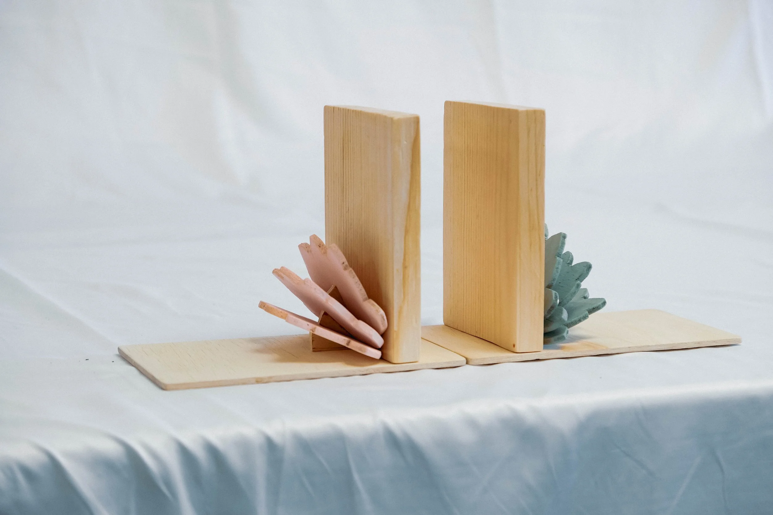 Abstract sculpture made of wooden blocks with pink and blue ceramic shells on a white fabric background.