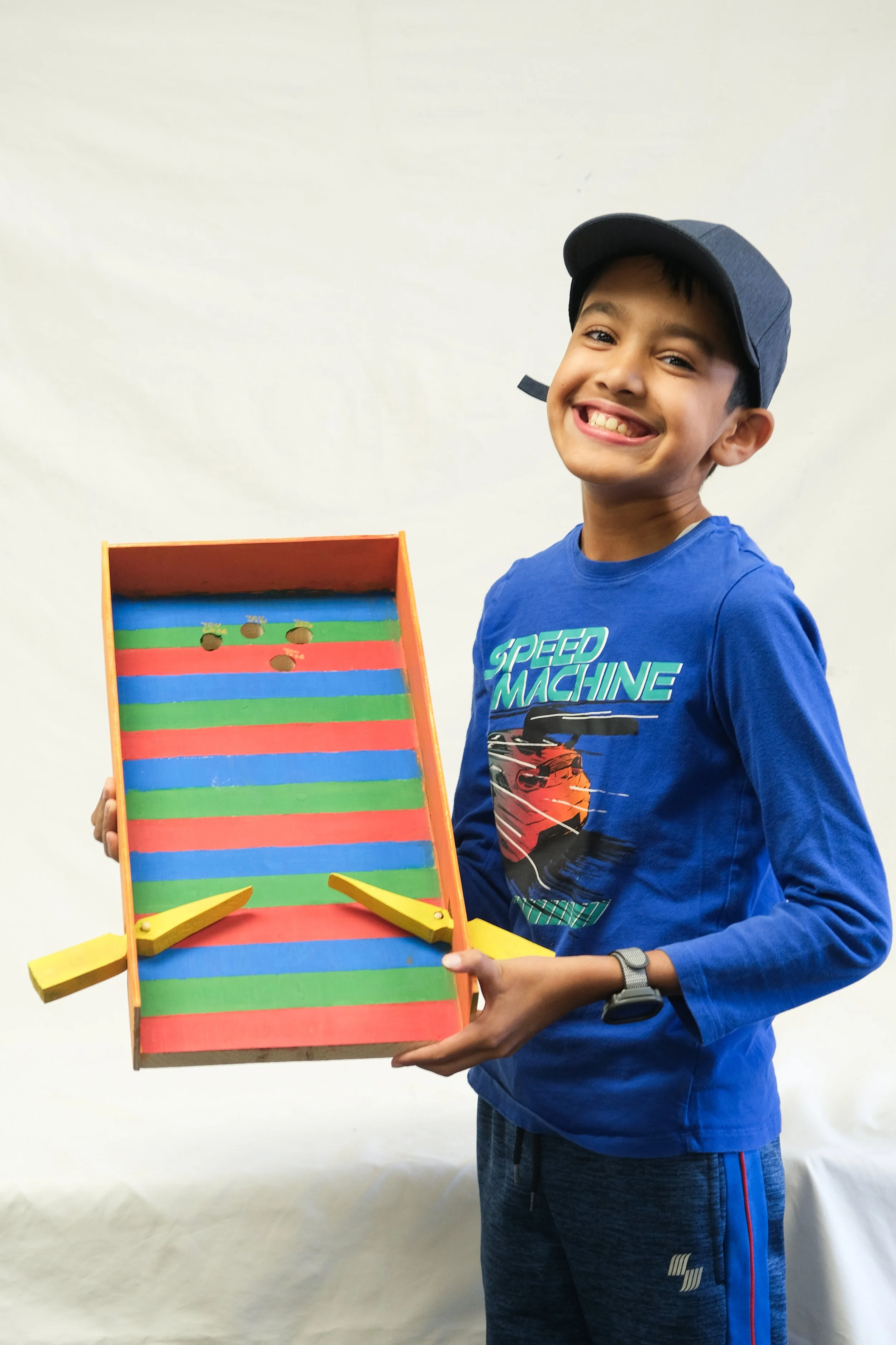 A boy smiling and holding a colorful wooden game with handles on each side, set against a plain background.