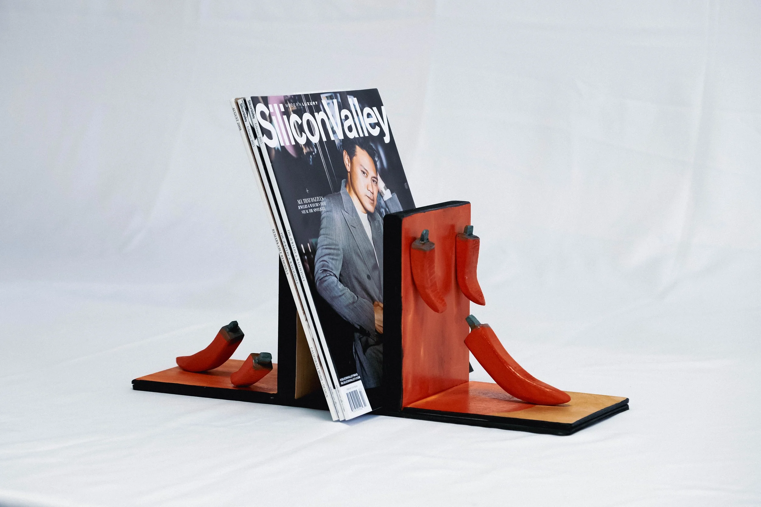 A magazine titled Silicon Valley leaning against a decorative wooden stand with red and black accents, with several small red shoe-shaped objects placed around it.