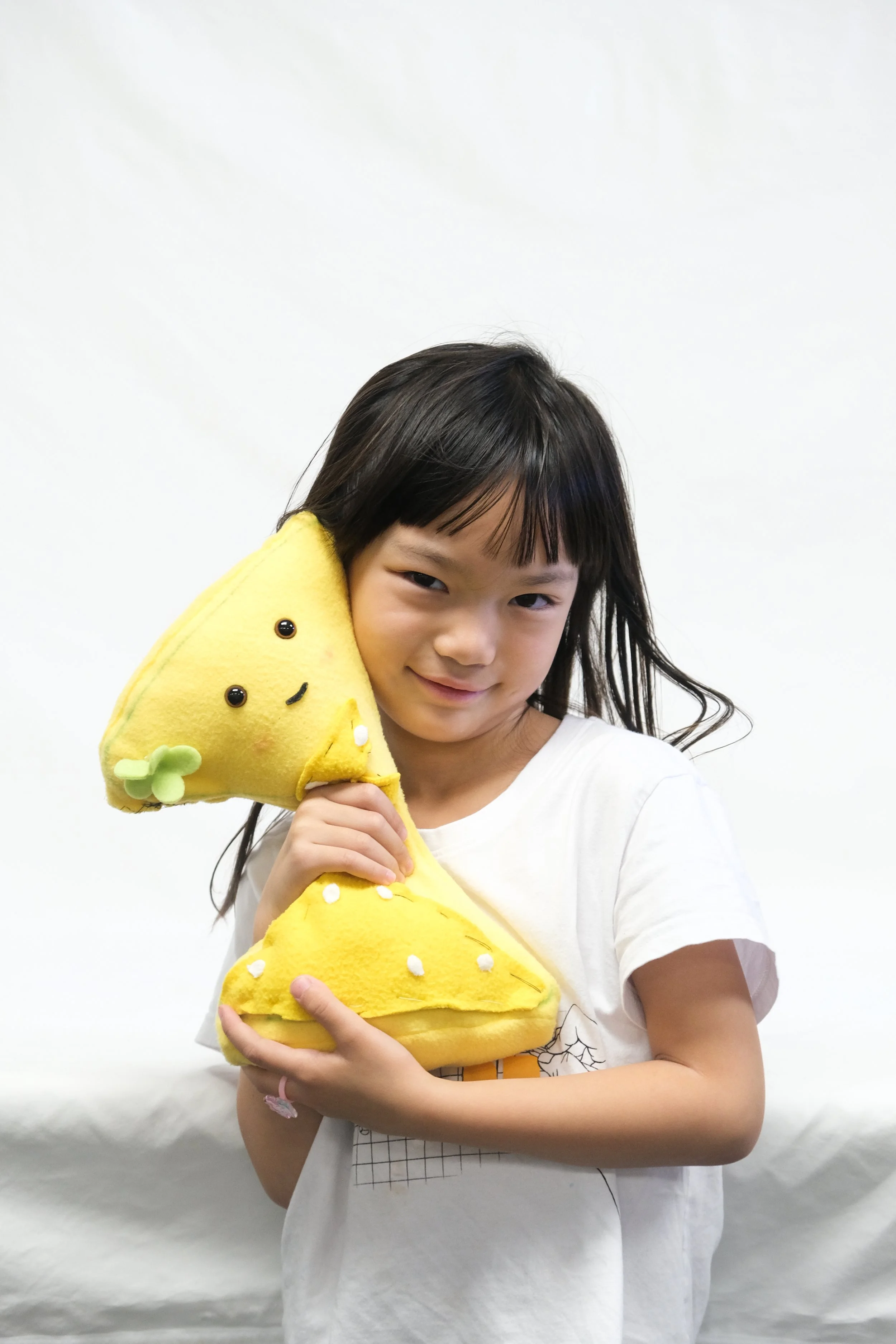 A young girl holding a yellow plush toy shaped like a smiling cheese wedge.