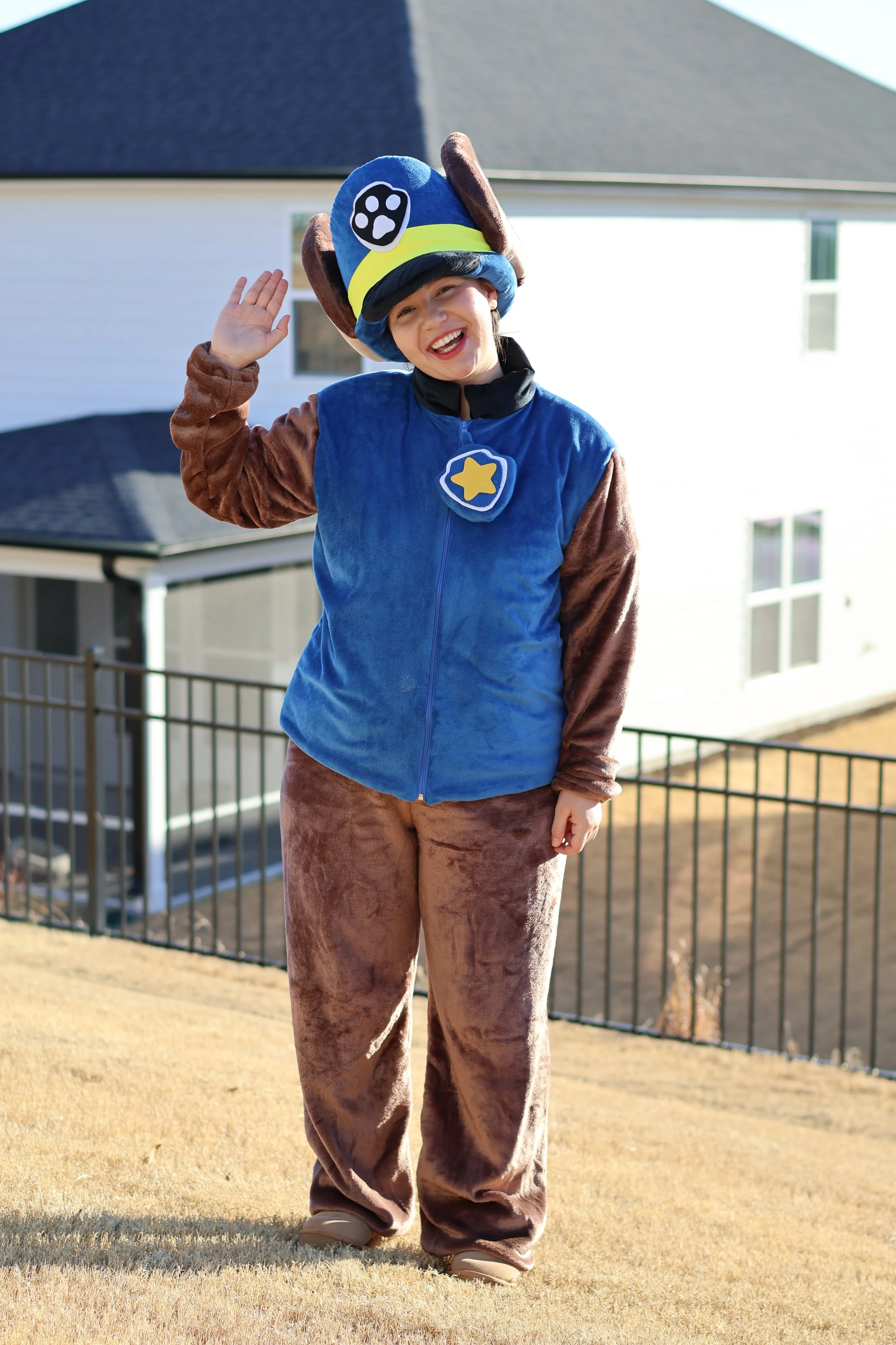 Person in a Paw Patrol costume standing outdoors, waving and smiling.