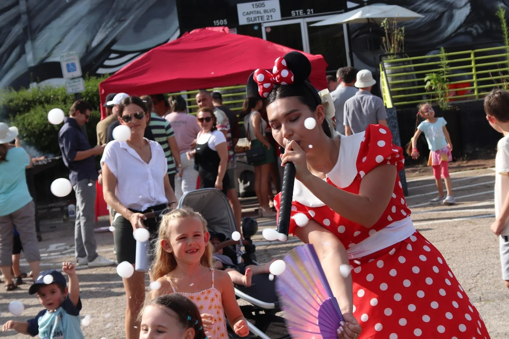 A woman dressed as Minnie Mouse blowing bubbles for children at an outdoor event.