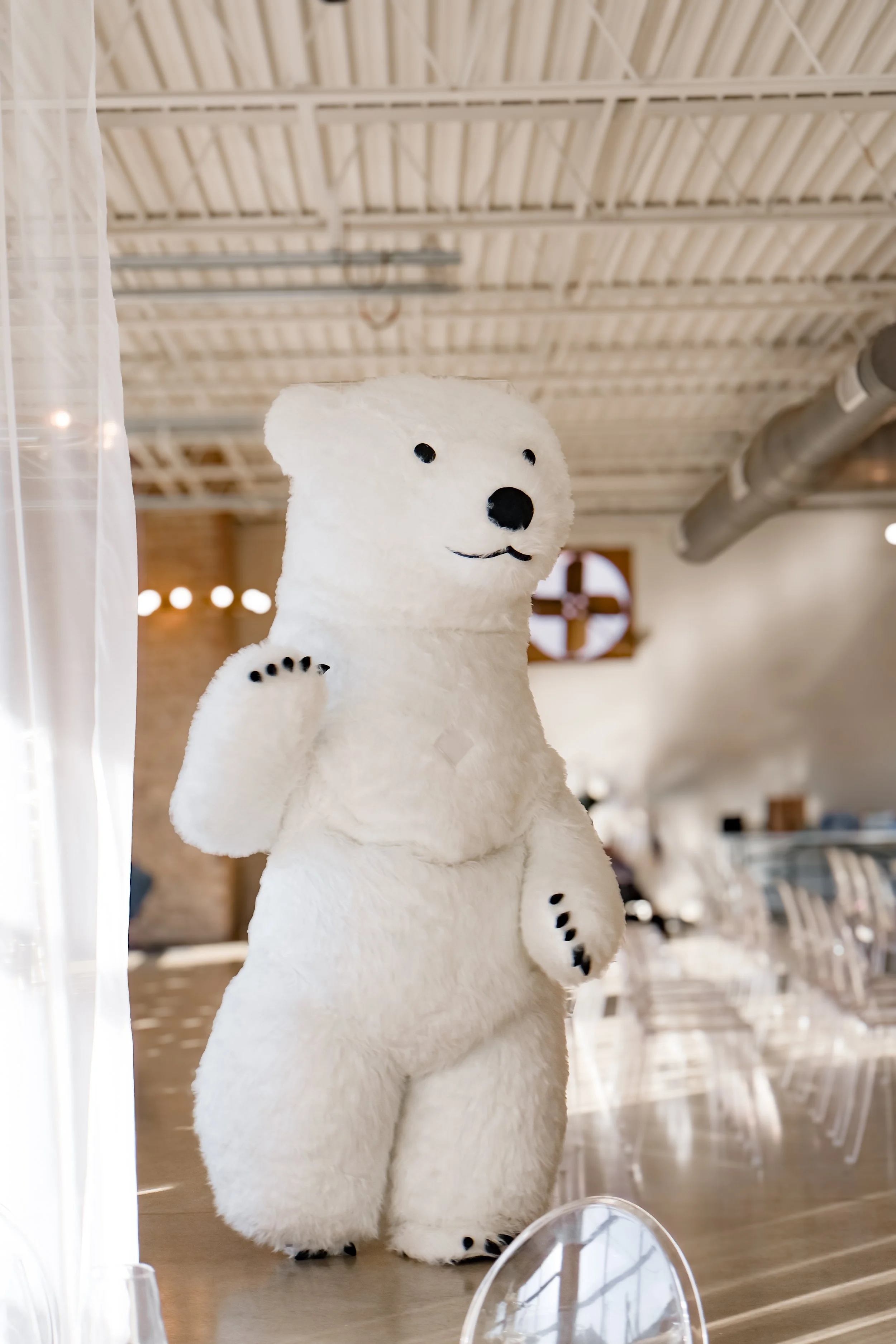 A person dressed in a large polar bear costume standing inside a modern, industrial-style room with a high ceiling and exposed ductwork.