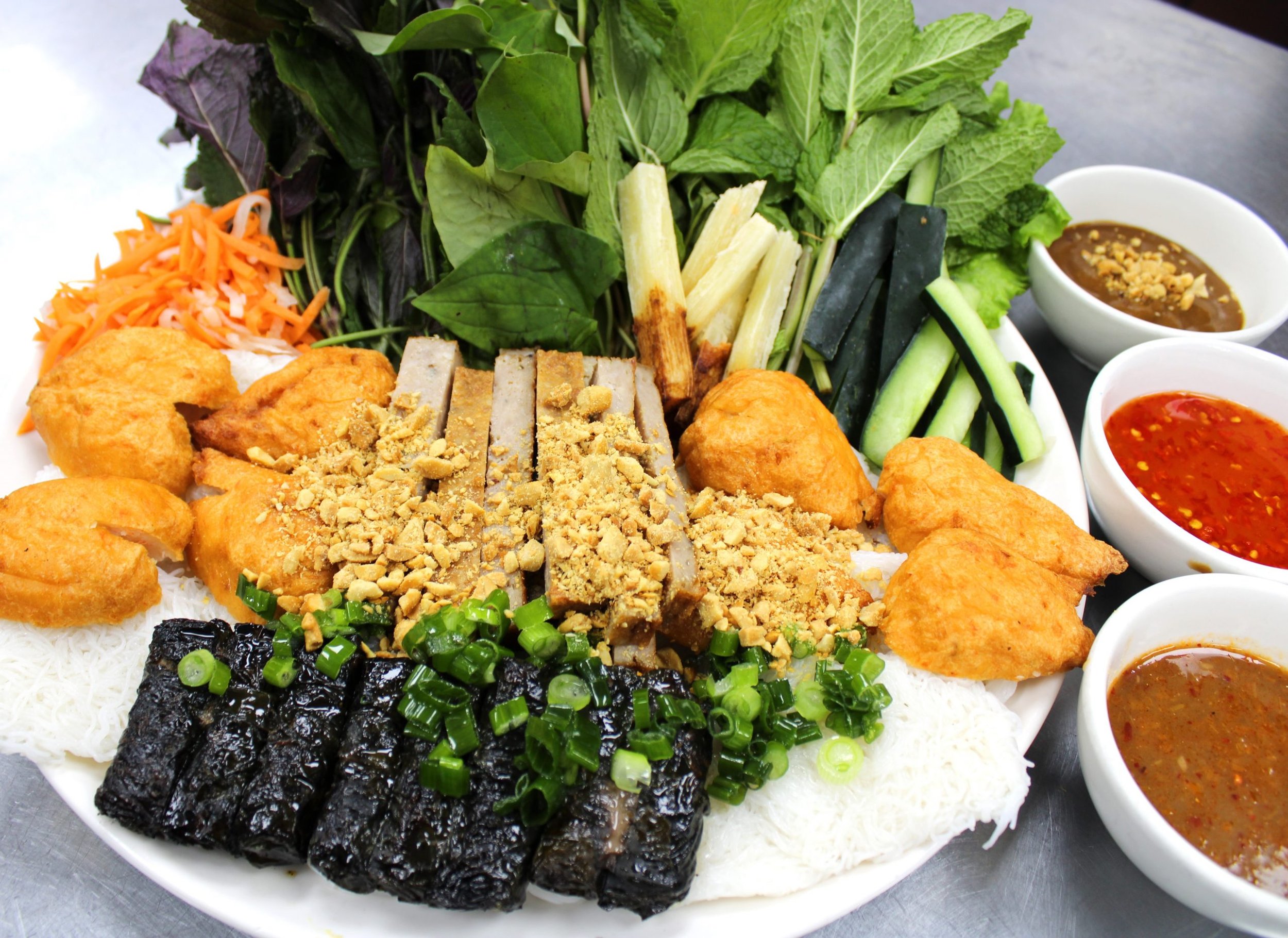Vietnamese cold cut platter with rice noodles, fresh herbs, vegetables, and dipping sauces.
