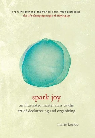 The book cover for 'Spark Joy: an illustrated master class to the art of decluttering and organising' by Marie Kondo, with a beige background and abstract green watercolour circle in the centre, and book title beneath