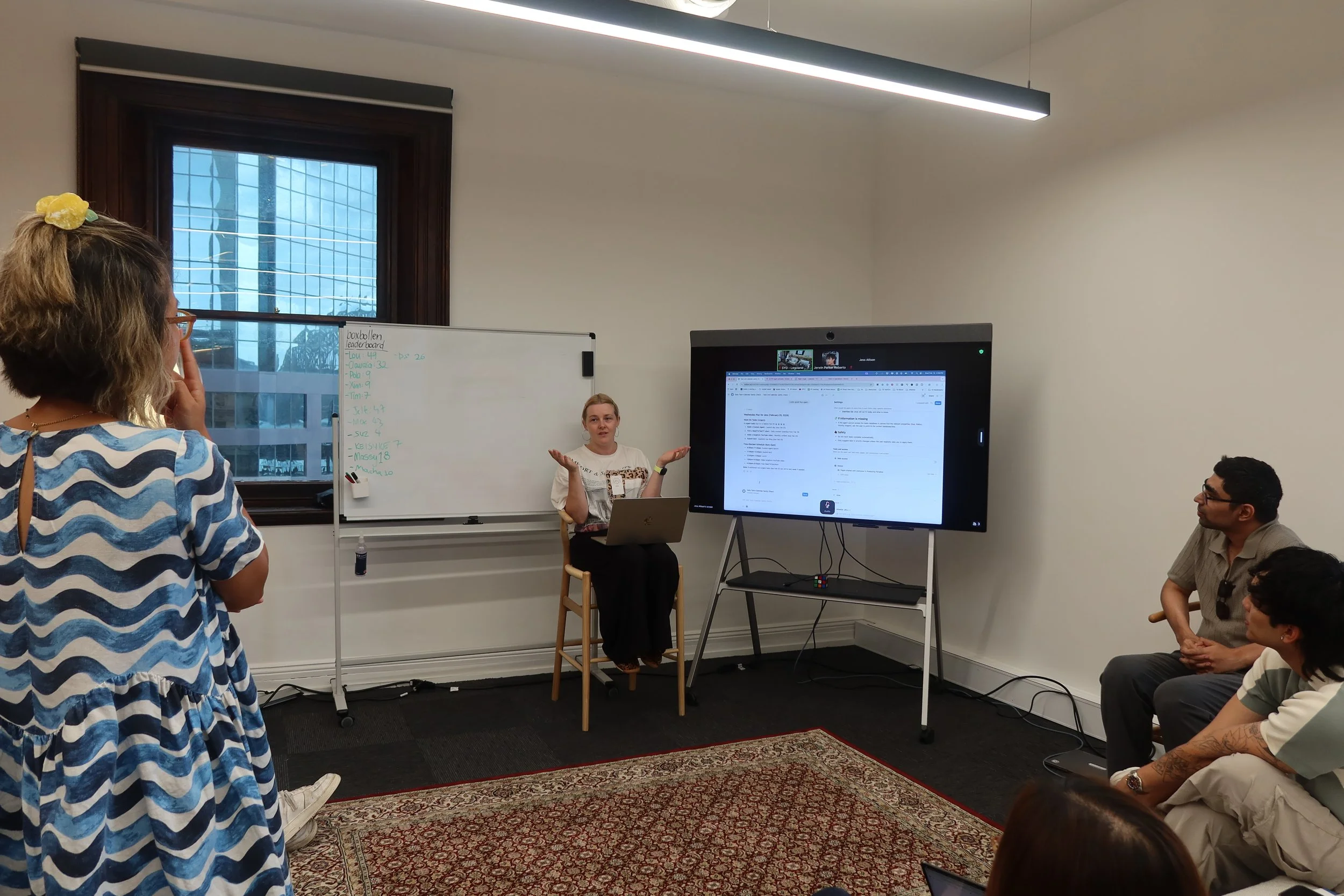 A woman speaking in front of a screen to a room full of people