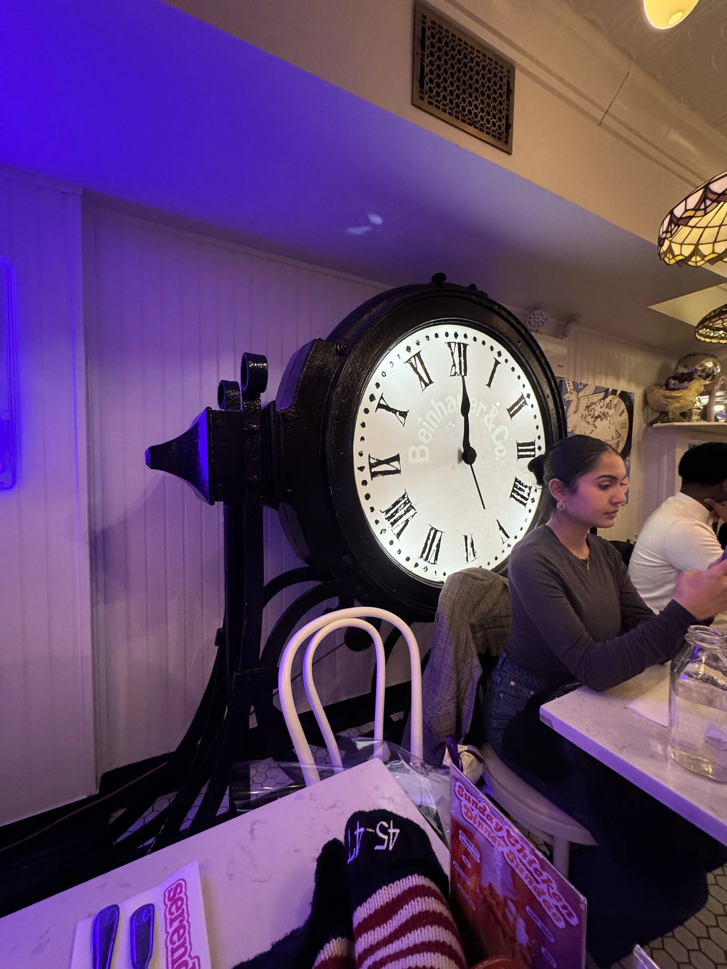 Vintage Clock from Serendipity Cafe in New York City, glowing under soft purple lights, a quiet moment of hope and fate just days before shouting love in Capital One Arena and getting the President to point back - frozen hot chocolate waiting