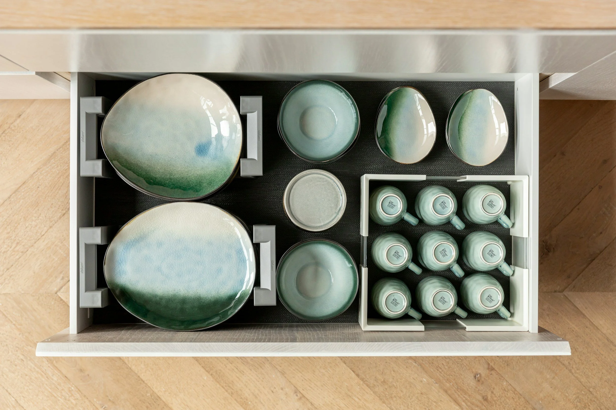 Open drawer containing green and cream colored ceramic plates, bowls, and mugs with a gradient pattern, arranged neatly.