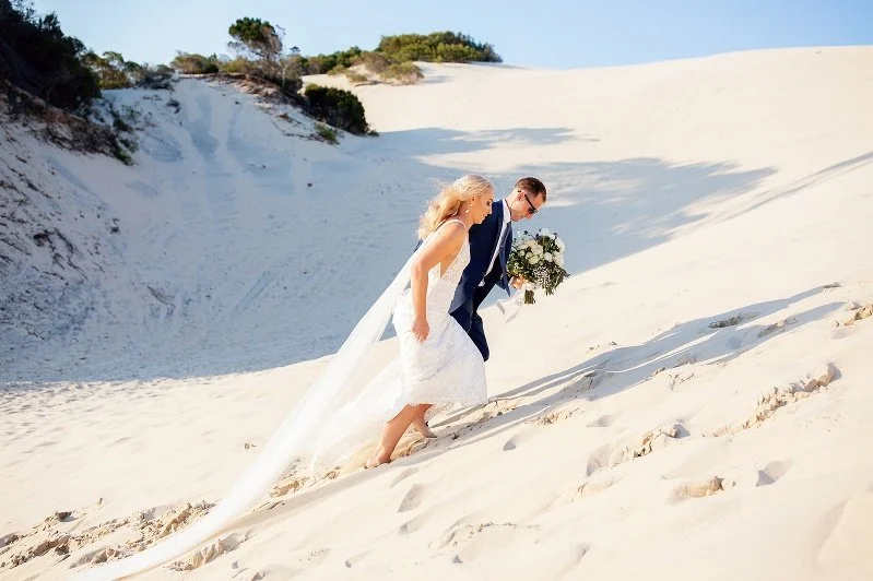 Bride and groom walking up a sandy dune at the beach photo by Lee Burgess from Love and Life Photography 