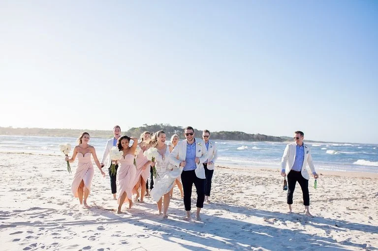 A wedding photo of a group of people dressed in wedding attire walking along the beach by Lee Burgess from Love and Life Photography 