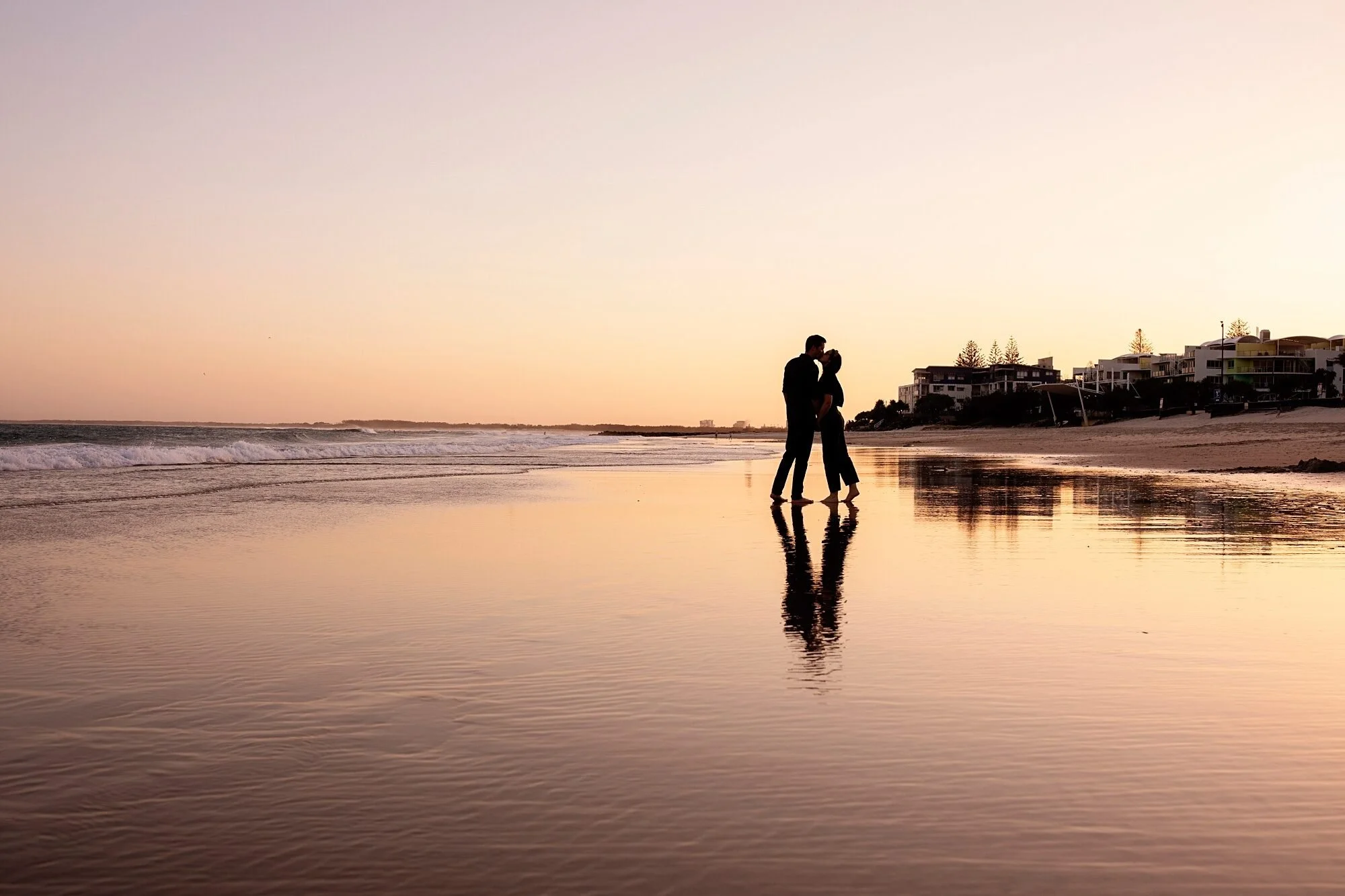 A photo of a couple stands on the beach at sunset by Lee Burgess from Love and Life Photography