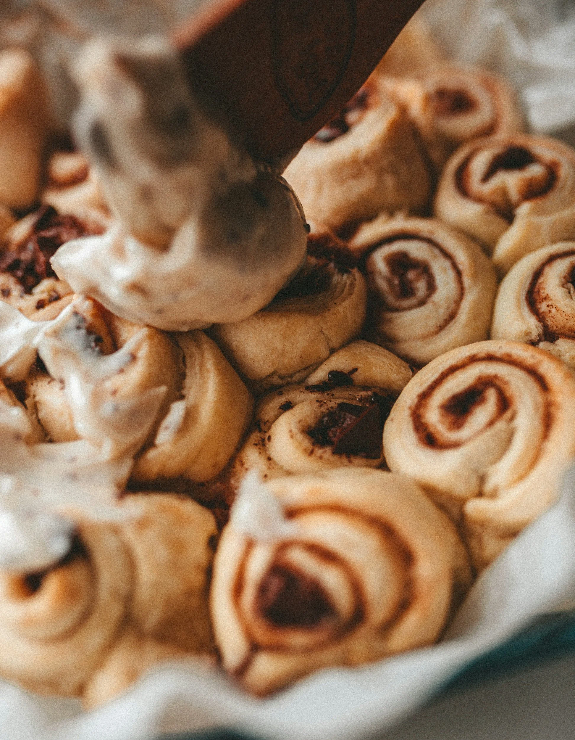 Close-up of vegan cinnamon rolls with icing being drizzled on top.