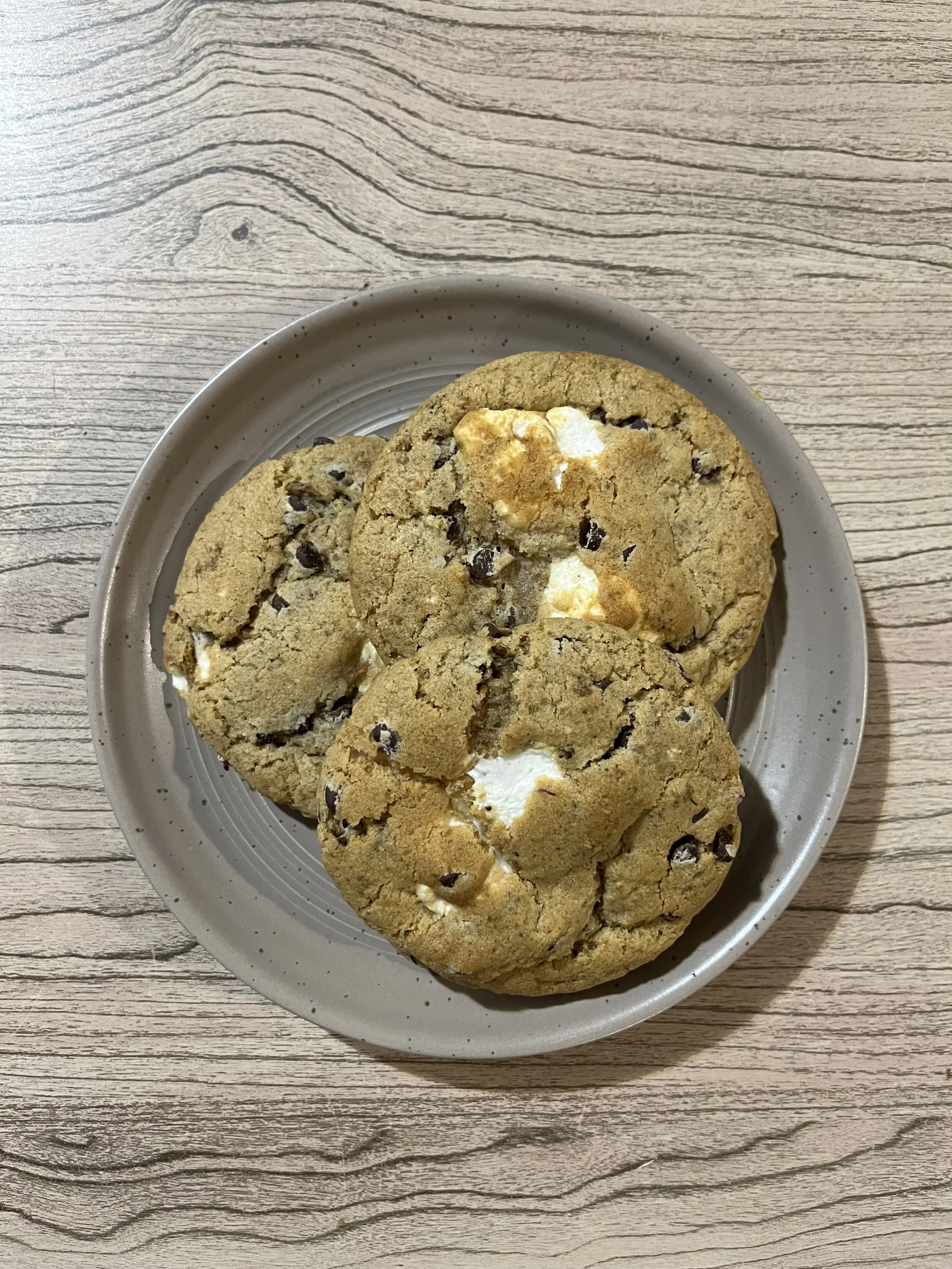 Three vegan s'more cookies on a grey plate, on a wooden table.