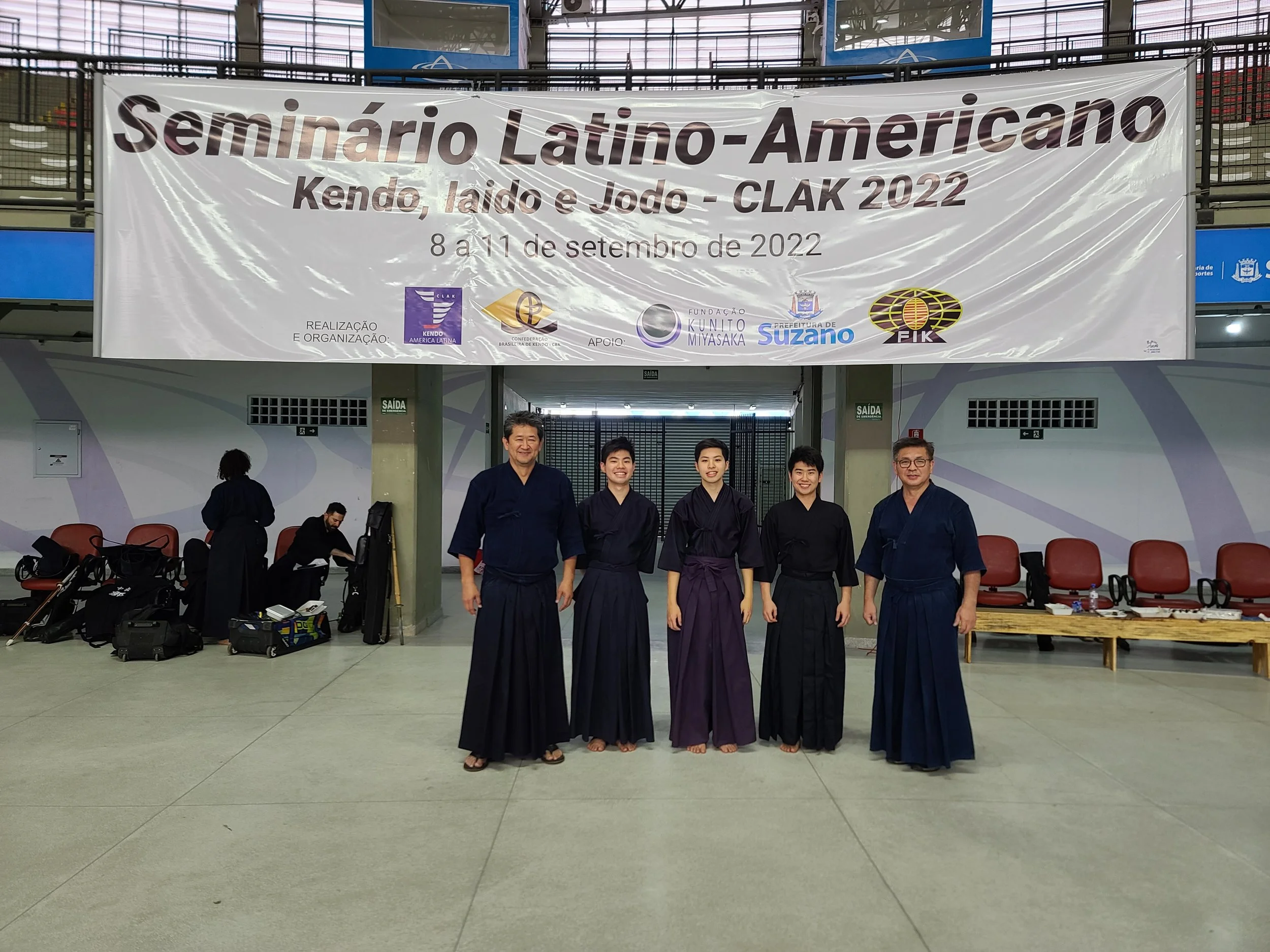 Group of five martial artists dressed in traditional kendo attire standing in front of a banner at a martial arts seminar.