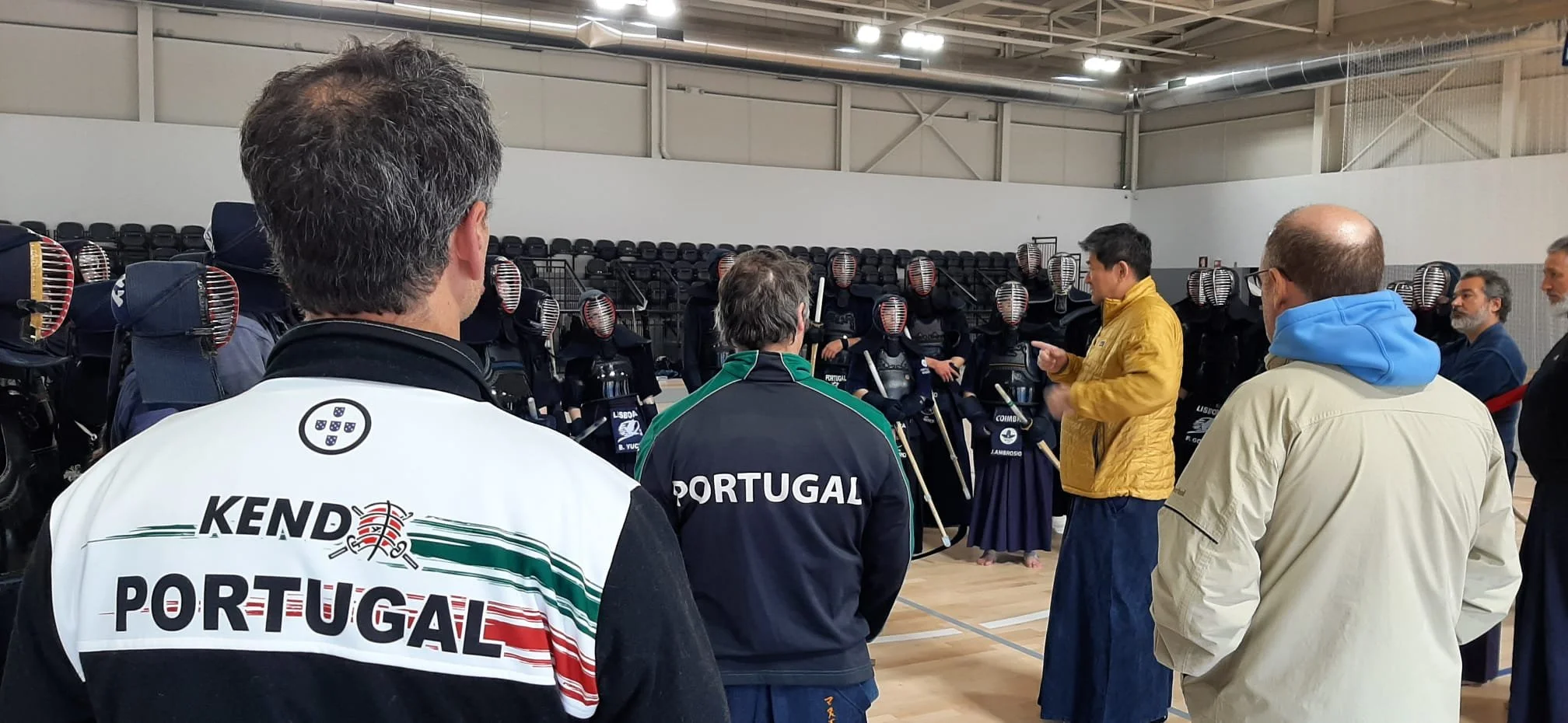 Group of people in casual clothing and kendo armor practicing kendo in a gym.