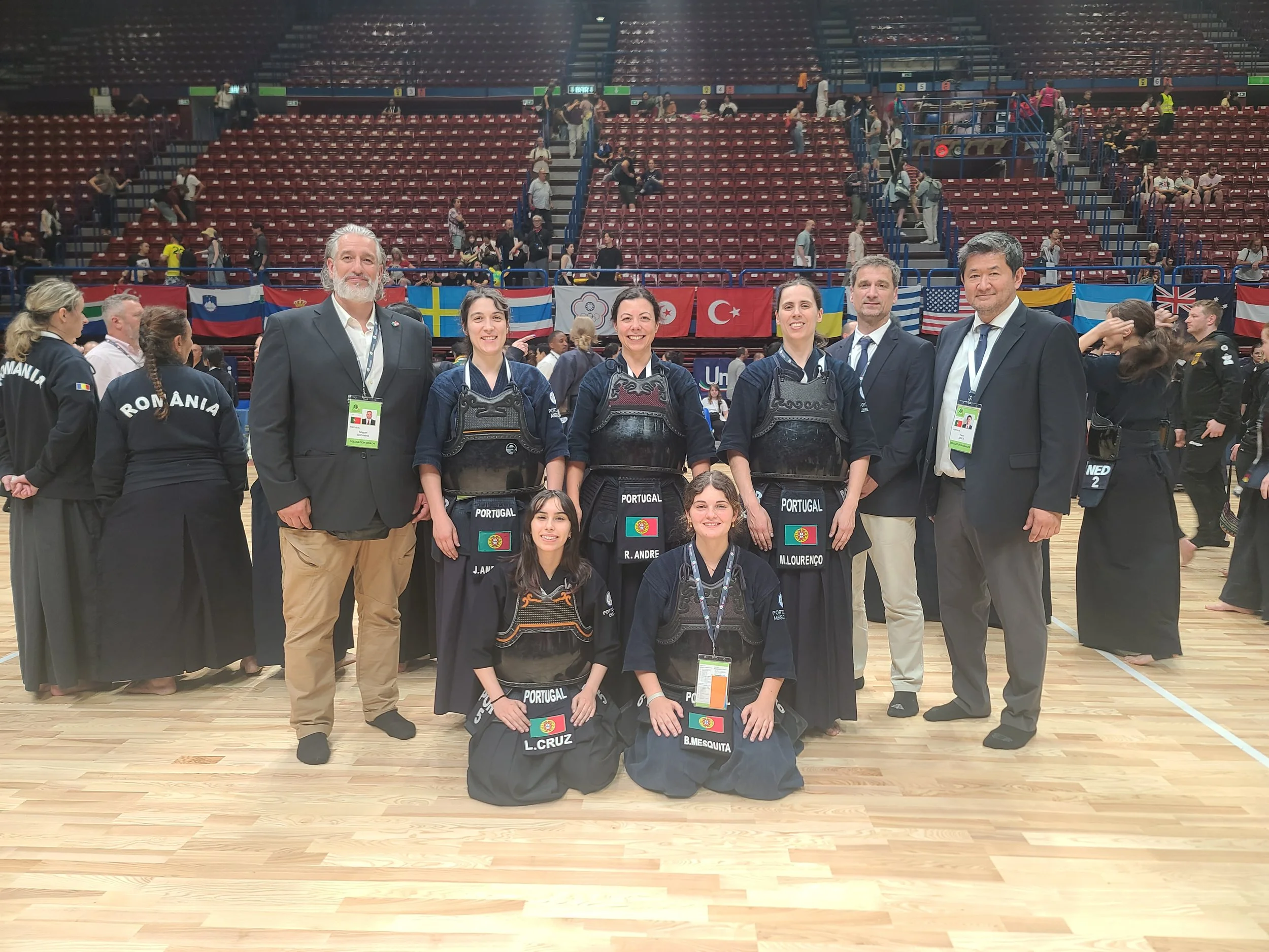Group of athletes and officials at a martial arts competition, with flags of Portugal and other countries in the background.