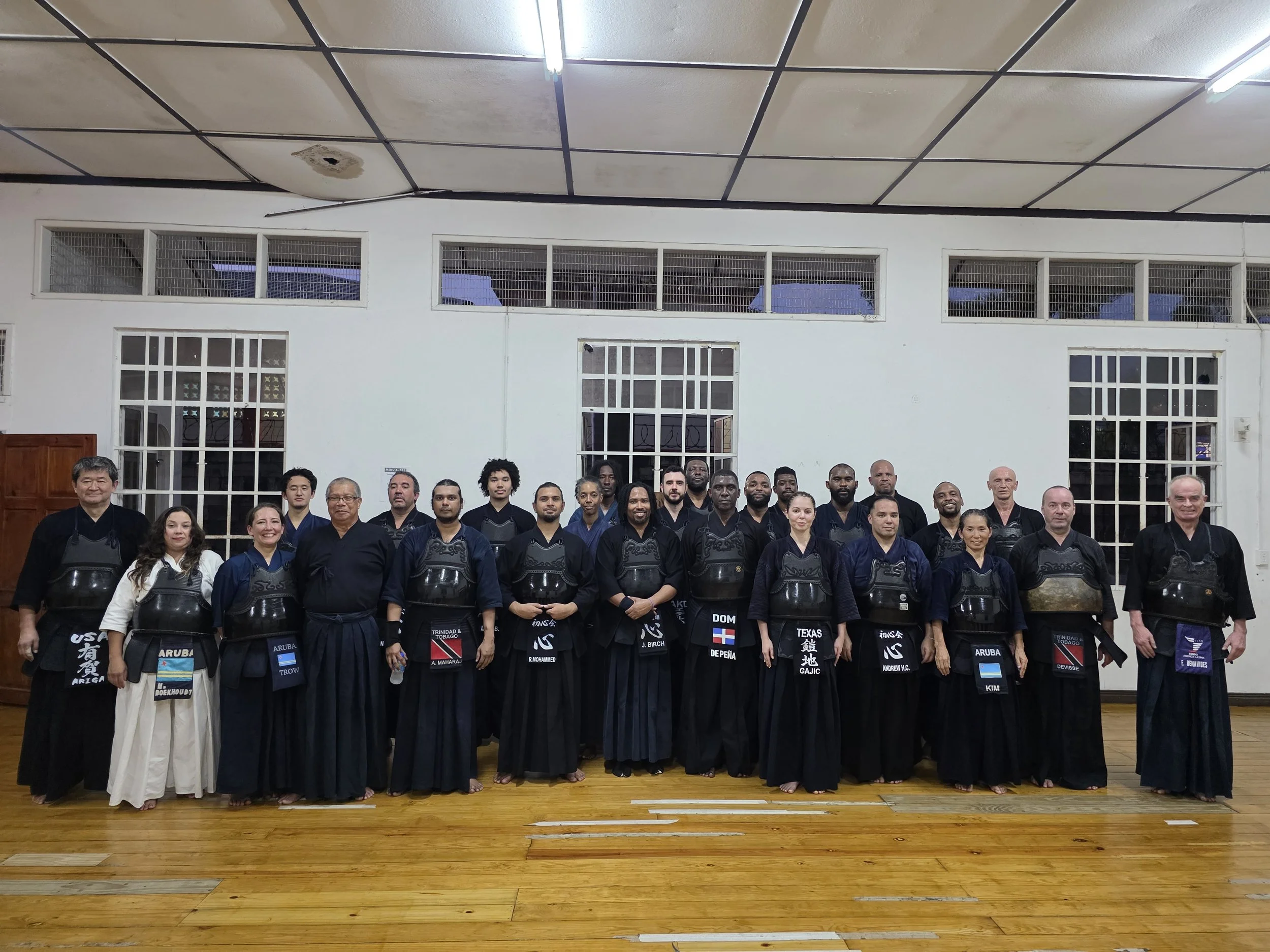 Group of individuals in martial arts uniforms, standing in a gymnasium.