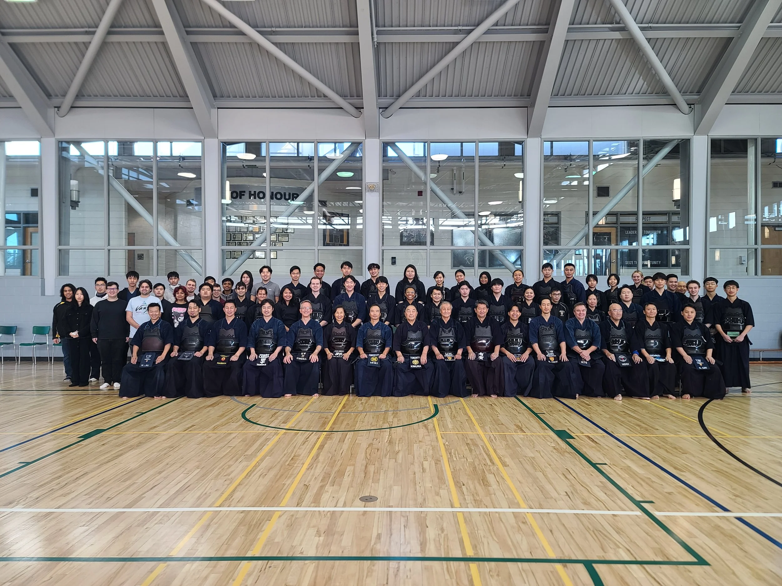 Group of people in martial arts uniforms and casual clothing posing for a photo in an indoor gymnasium.