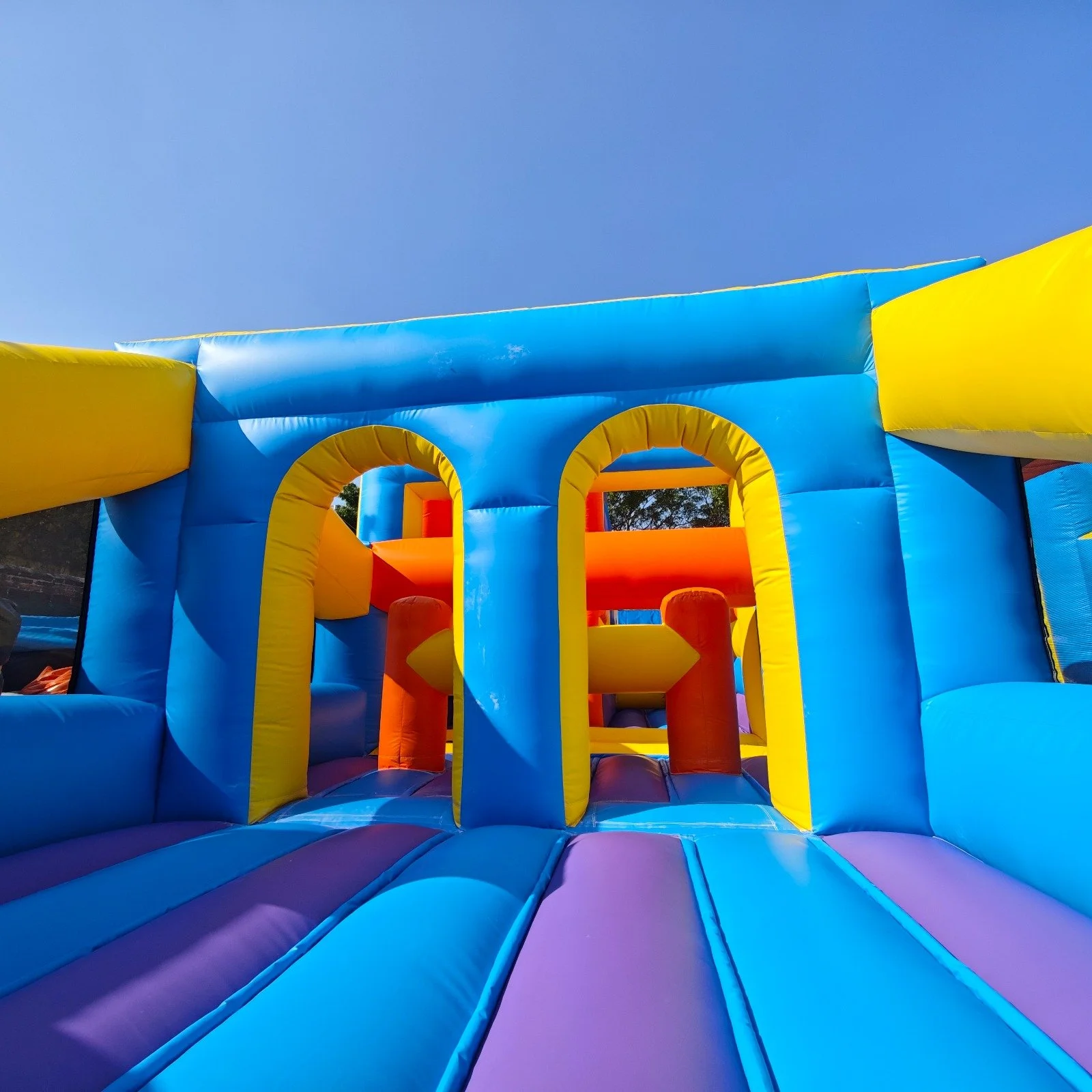 Colorful inflatable bounce house with arches and slides under a clear blue sky.