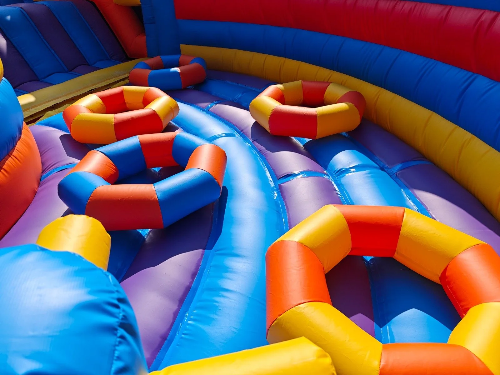 Colorful inflatable bounce house with rainbow colors and obstacle rings.