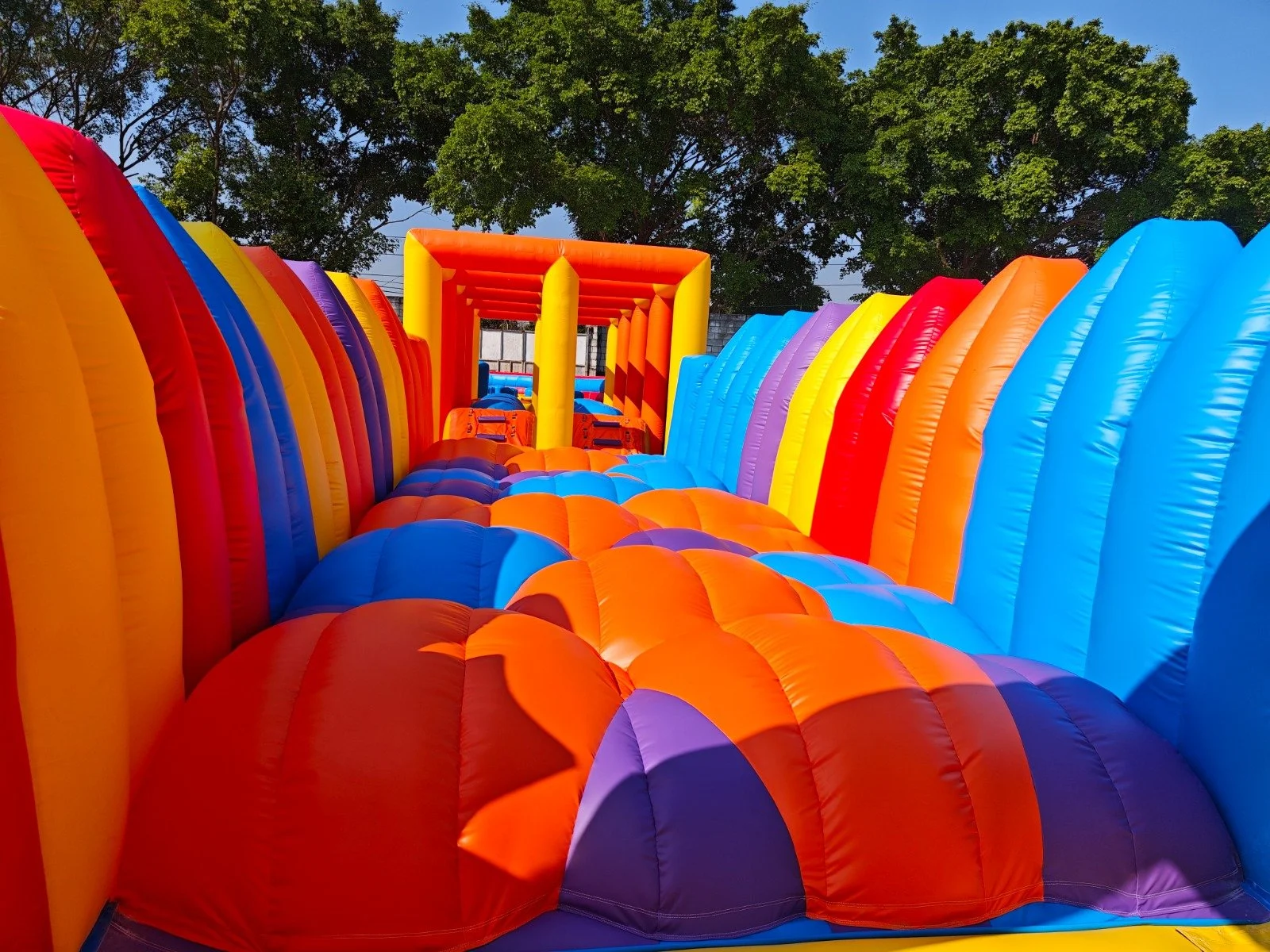 Colorful inflatable obstacle course set outdoors under green trees.
