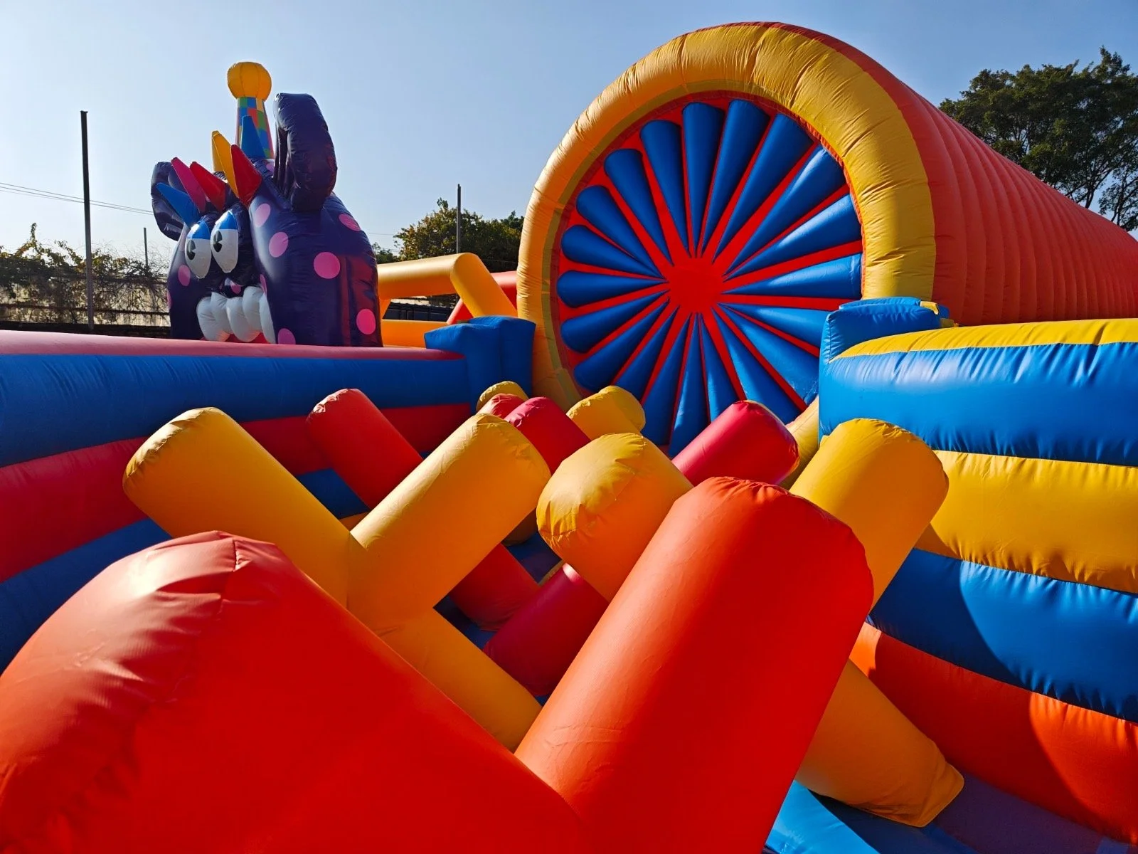 Colorful inflatable bounce house with a purple cat face and large blue and red wheel design, set outdoors on a sunny day.