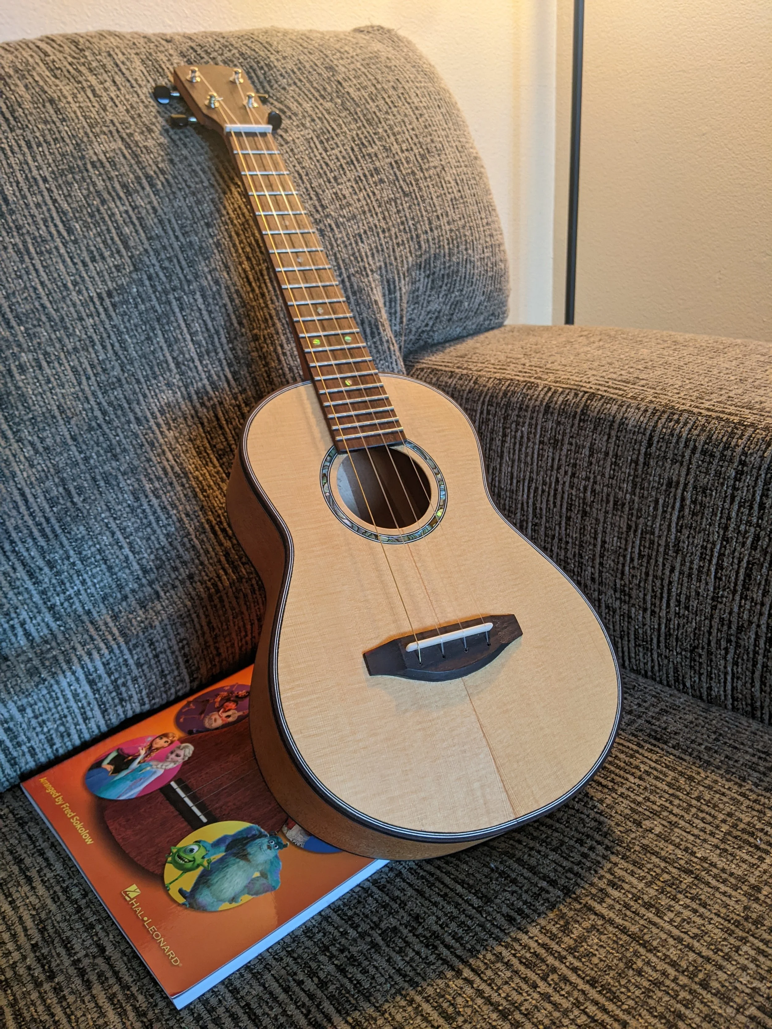 Tenor ukulele on a couch. It has a spruce top and mahogany sides.