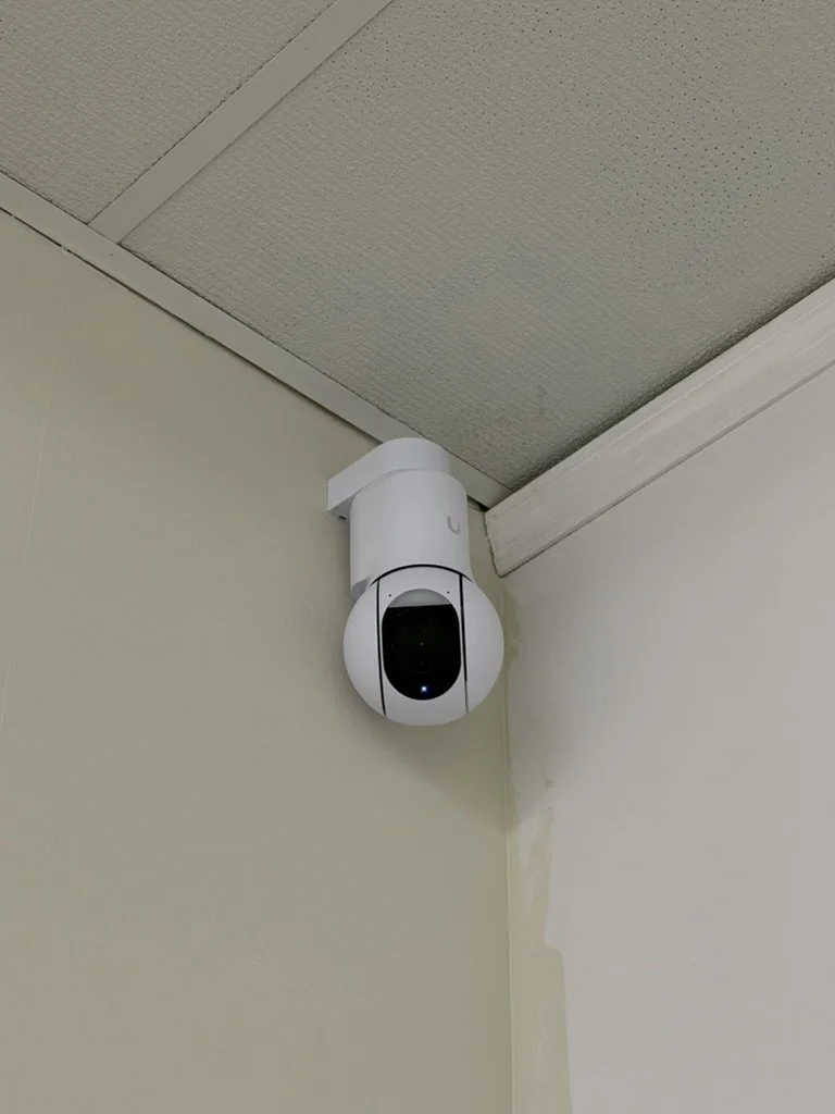 A white security camera mounted in the upper corner of a room.