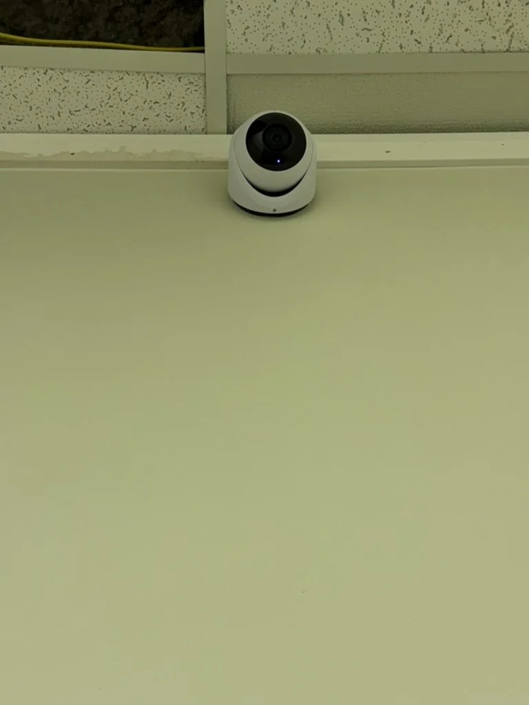 A white security camera mounted on a green wall.