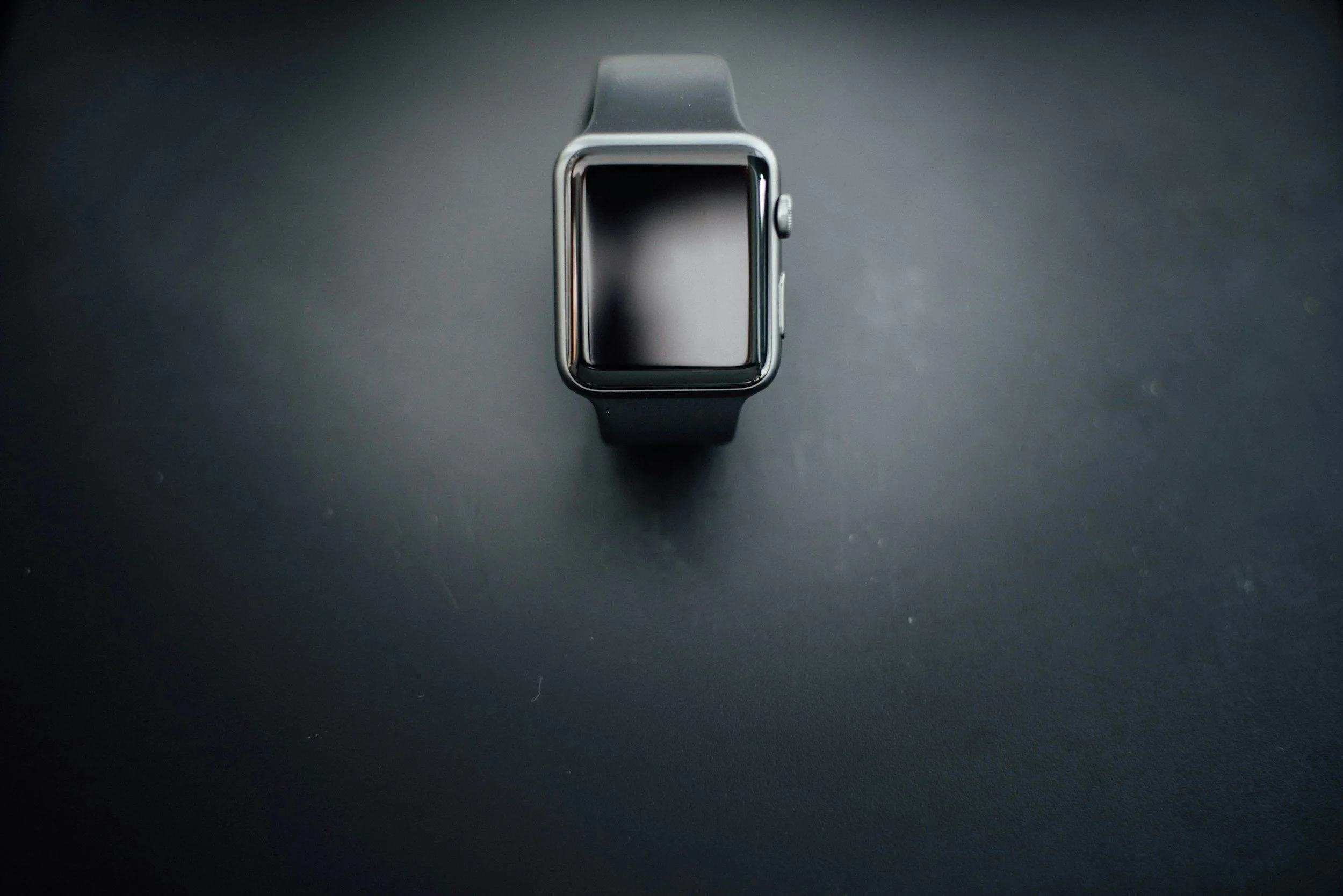 An Apple Watch with a black band on a black surface.