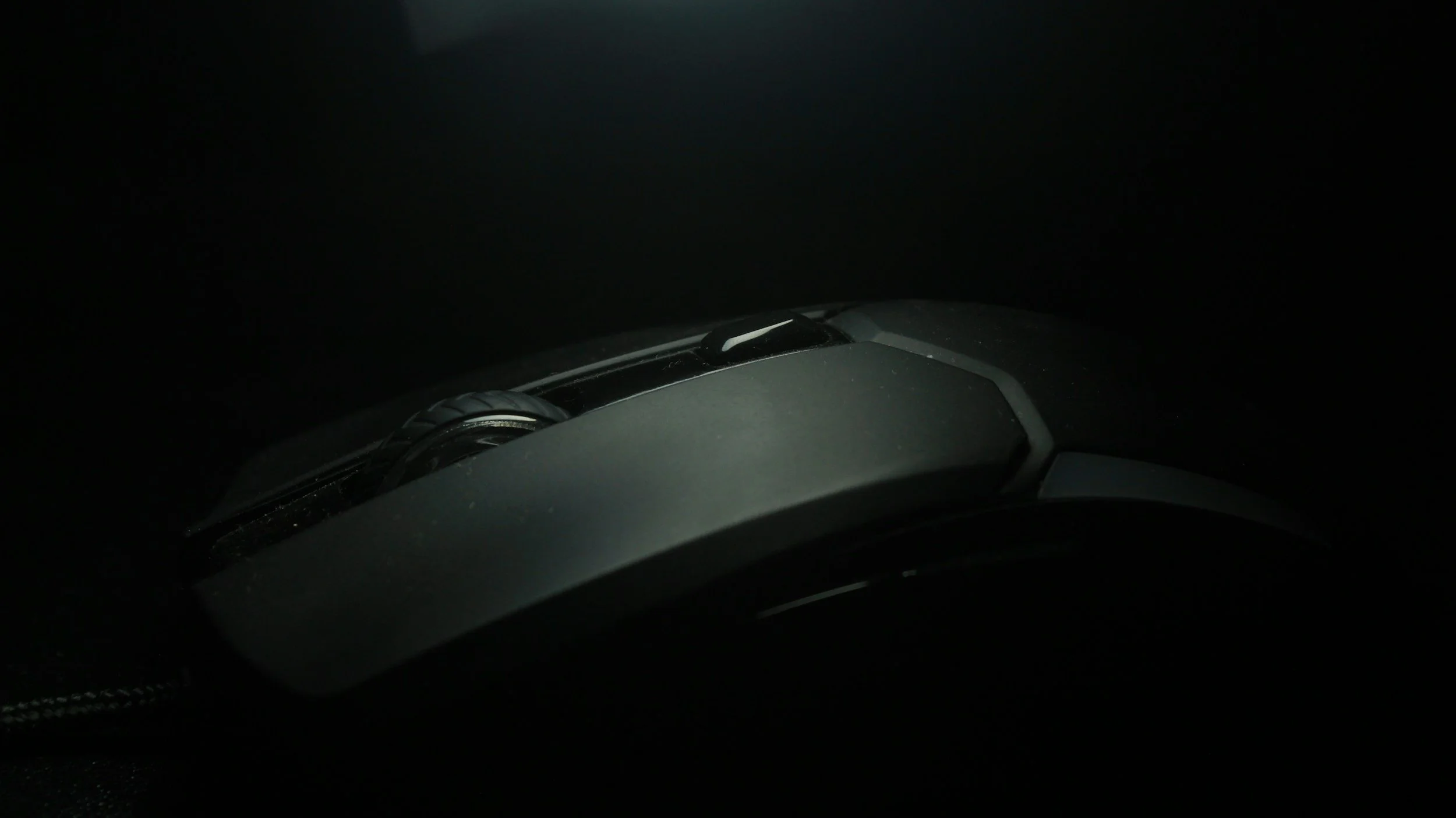 Close-up of a computer mouse in a dark environment with a light source highlighting its surface.