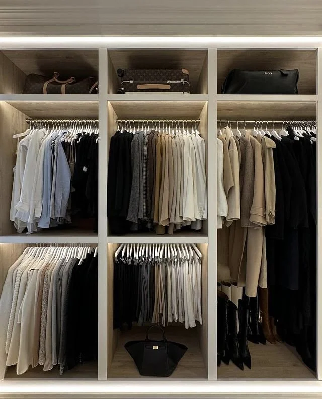 A neatly organized closet with shelves and hanging sections for clothes and accessories, featuring suits, sweaters, and handbags.