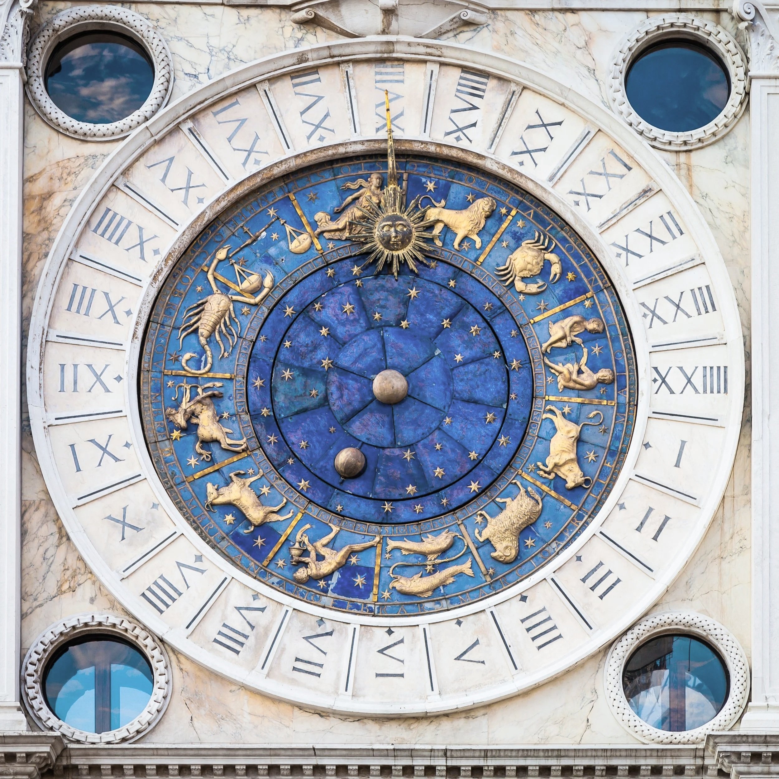An ornate astronomical clock with zodiac signs and Roman numerals, set against a marble building facade.