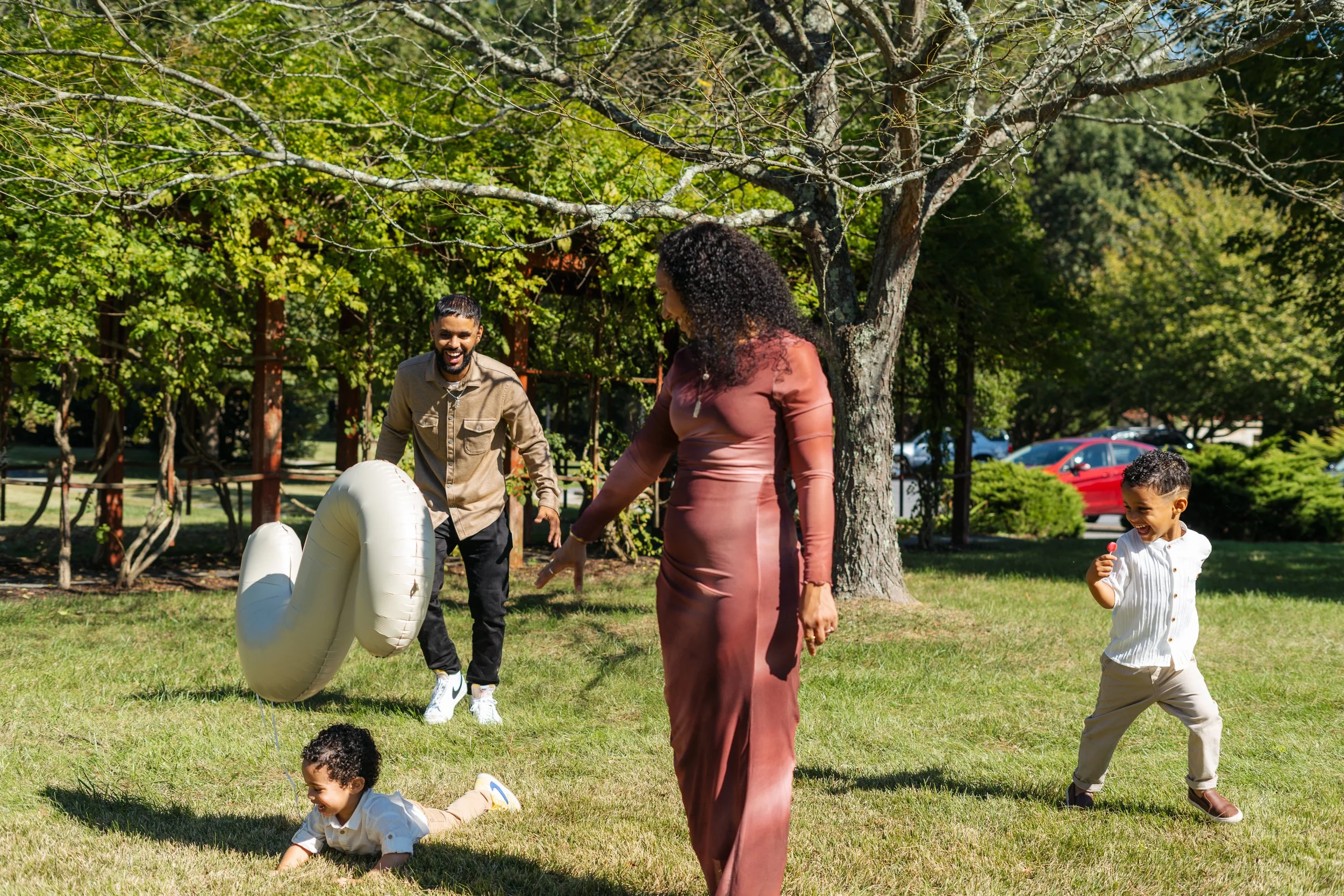 Family enjoying a game of ring toss in a park on a sunny day, with trees and parked cars in the background.