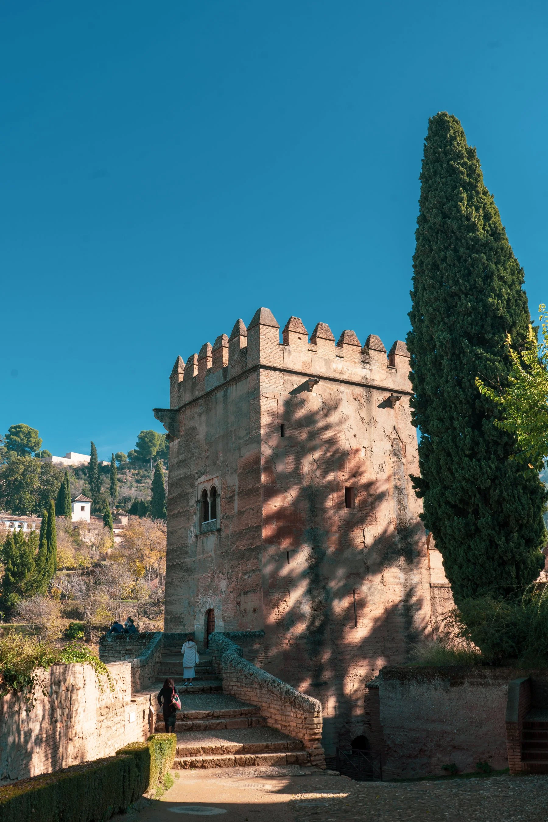 An old stone tower with a crenelated top, surrounded by trees and a blue sky.