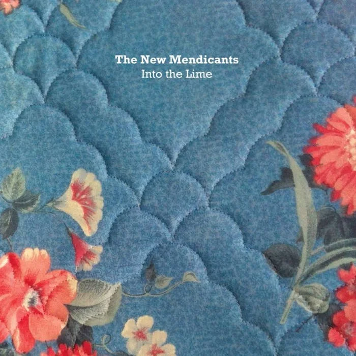 Close-up of a blue mattress fabric with quilted pattern, featuring red, white, and pink flowers and green leaves, with the text "The New Mendicants Into the Lime" at the top center.