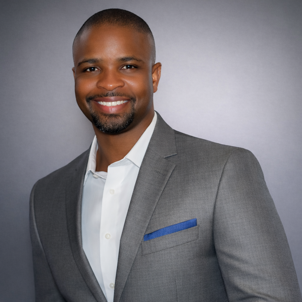 A smiling African American man in a gray suit and white shirt against a gray gradient background.