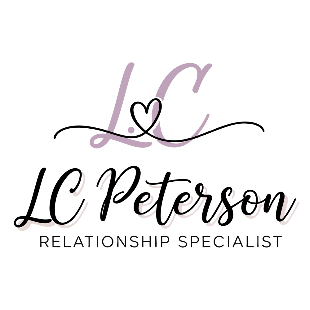 A lavender gift box with a black ribbon tied into a bow, with a black heart-shaped tag attached, placed on a reflective surface.