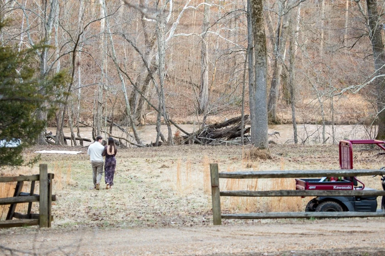 Caroline and Clay walking hand-in-hand through the woods after their surprise proposal near Richmond, Virginia.
