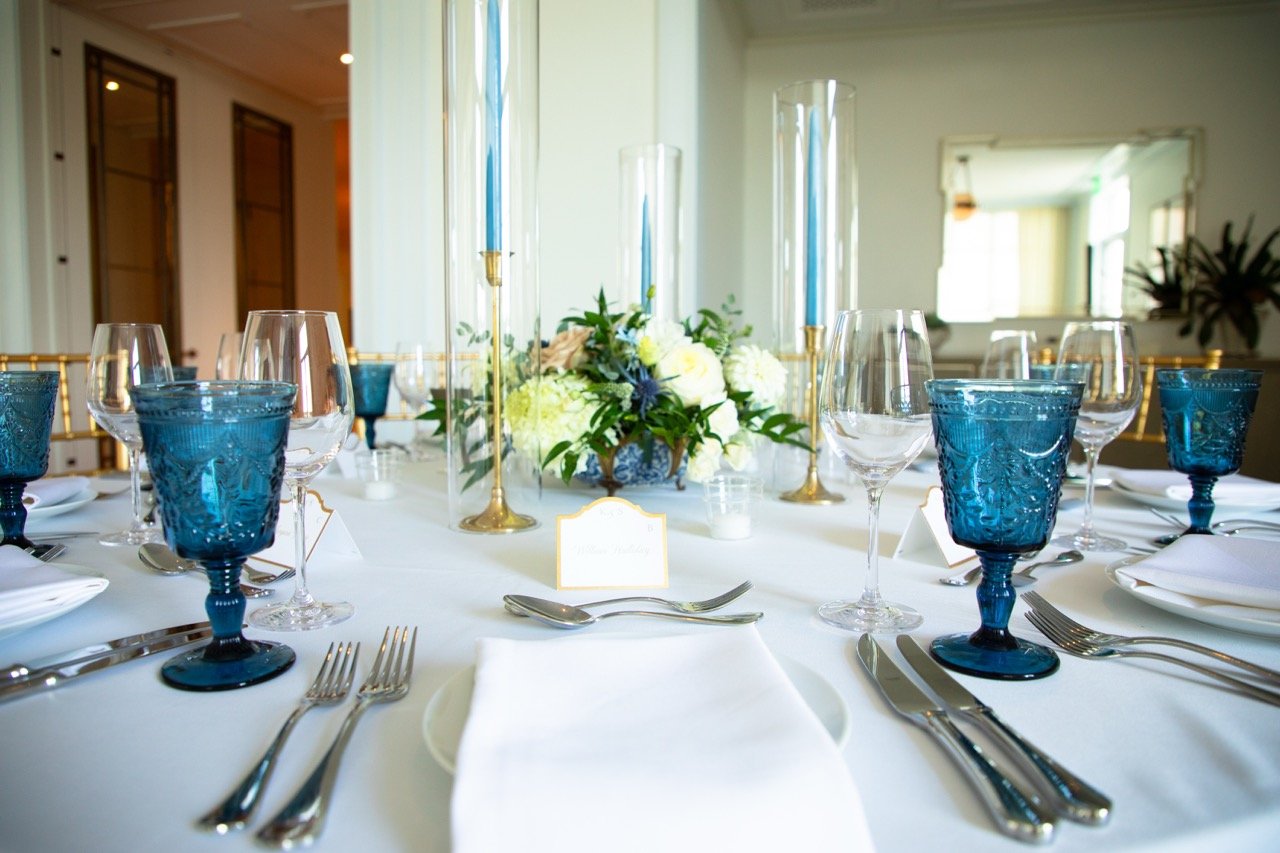 Beautifully curated ballroom space featuring round dinner tables styled in clean white linens and blue accent glassware.