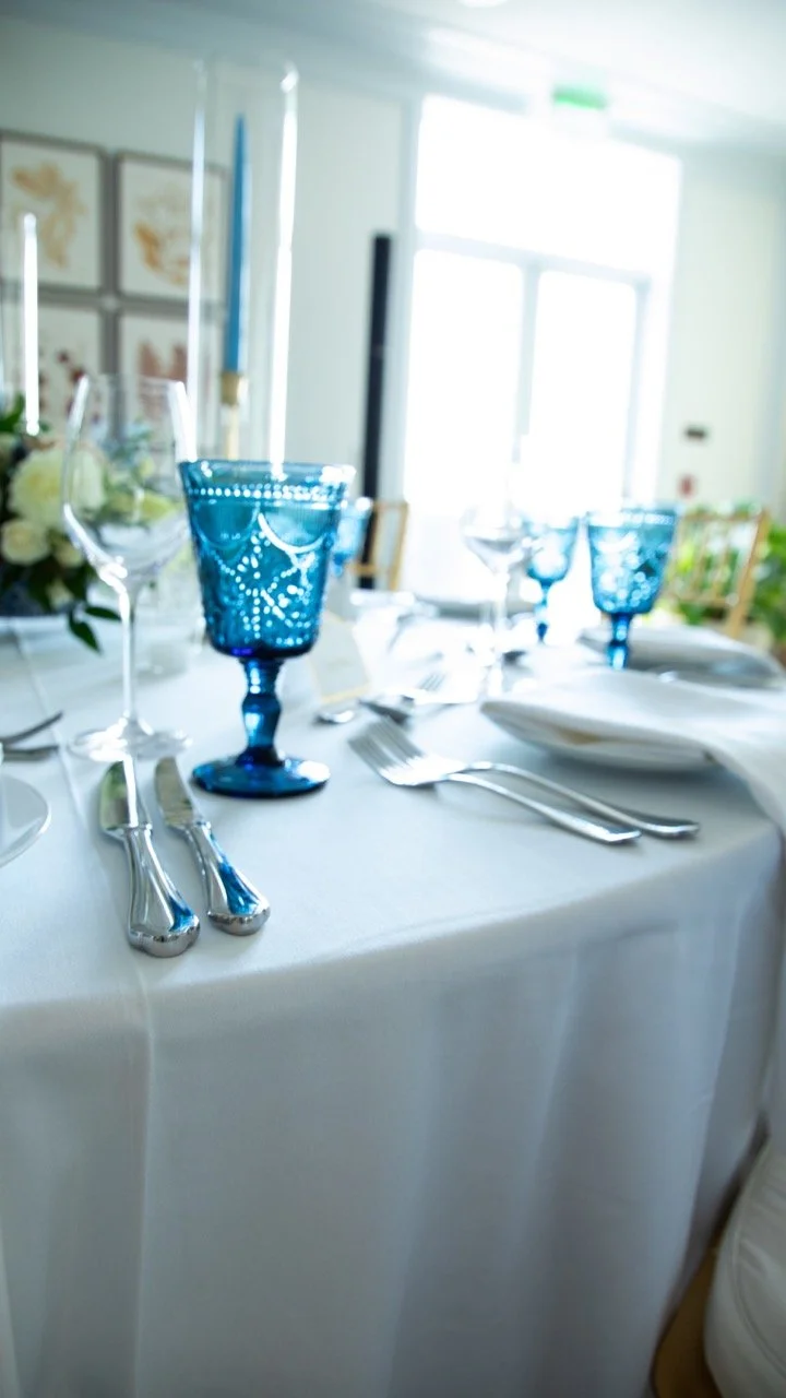 Polished silverware alongside cobalt blue vintage goblets on a clean white tablecloth at a formal dinner space.