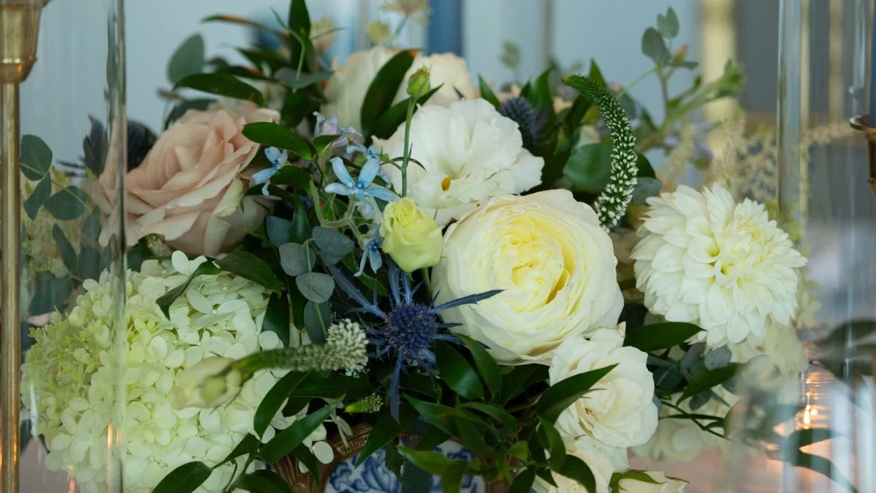 Stunning floral design close-up showing white dahlias, ivory roses, and soft seasonal textured greens.