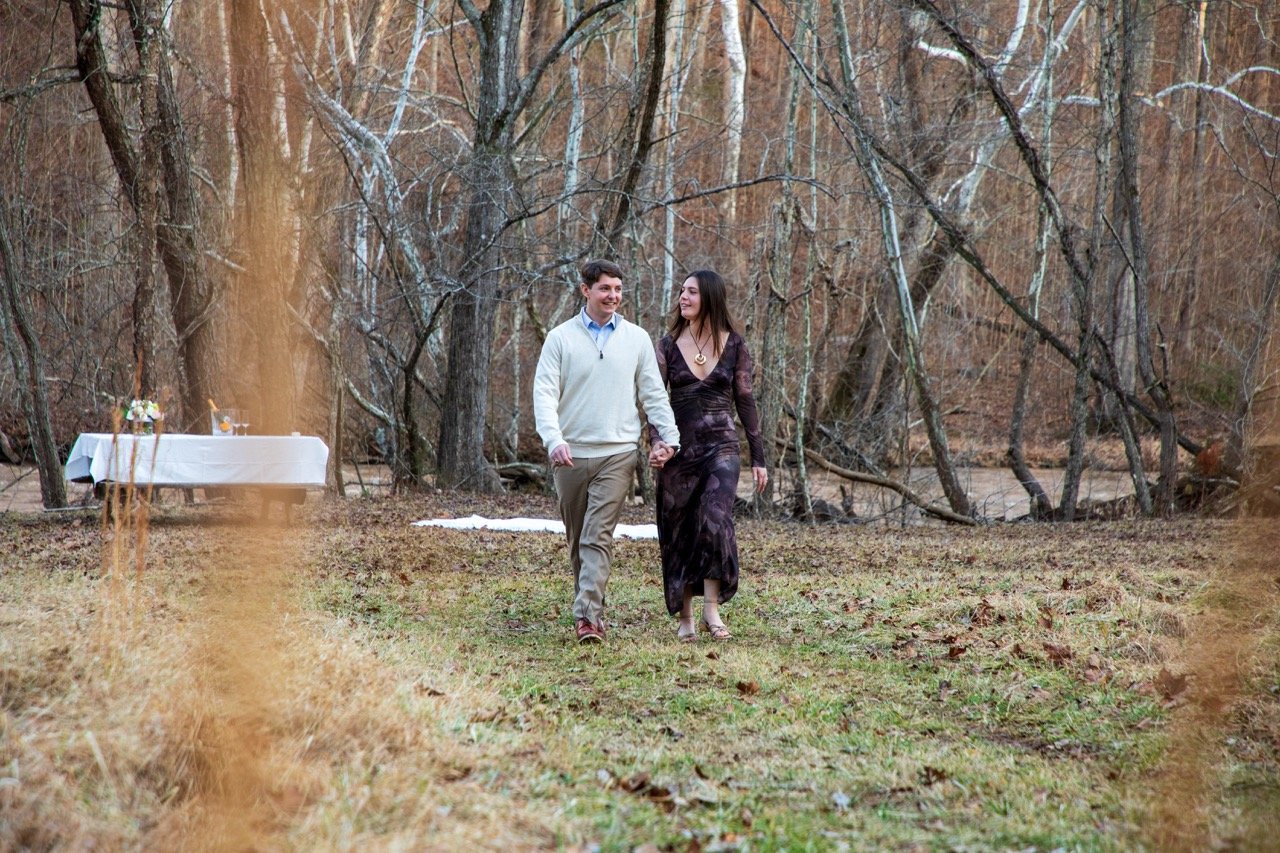 A classic, joyful engagement portrait of a couple walking through a forest trail, captured by a NoVA wedding photographer.