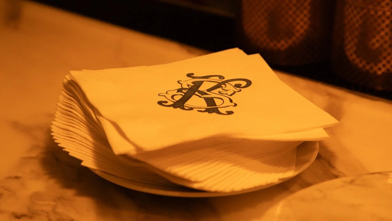 Custom monogrammed cocktail napkins featuring a classic black embroidered "R" initial for a rehearsal dinner bar setup.