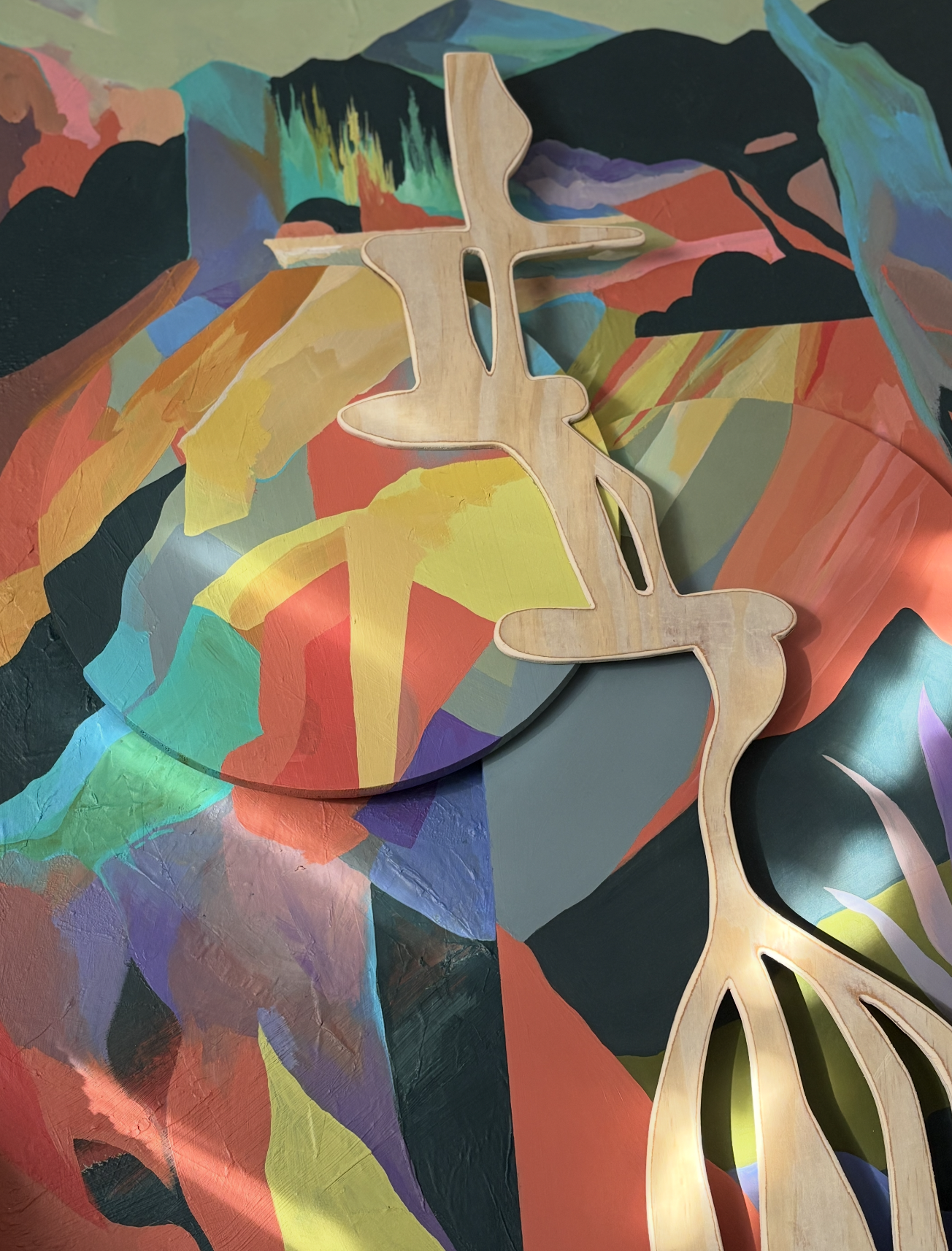 Colorful, abstract painted surface with cutout wooden decorative object.