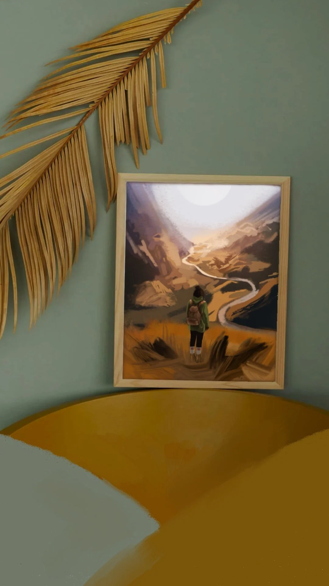 A framed artwork on a teal wall depicting a person standing on a trail overlooking winding river and mountains, with a large gold leaf decoration and part of a yellow bed at the bottom of the image.