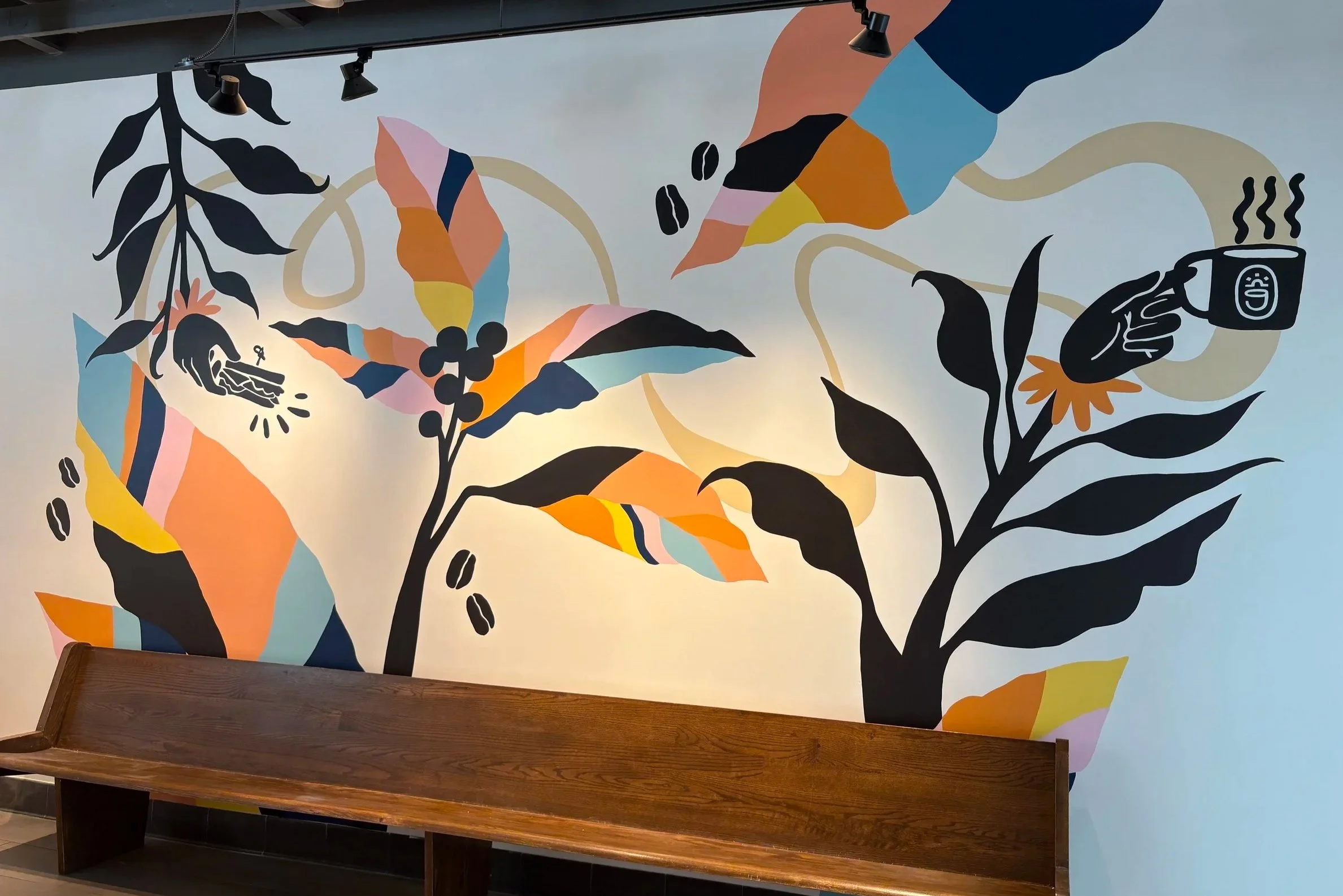 Wall mural of abstract black and colorful plant illustrations, including leaves, berries, and coffee beans, with coffee cup and hand holding coffee, and a wooden bench in front.