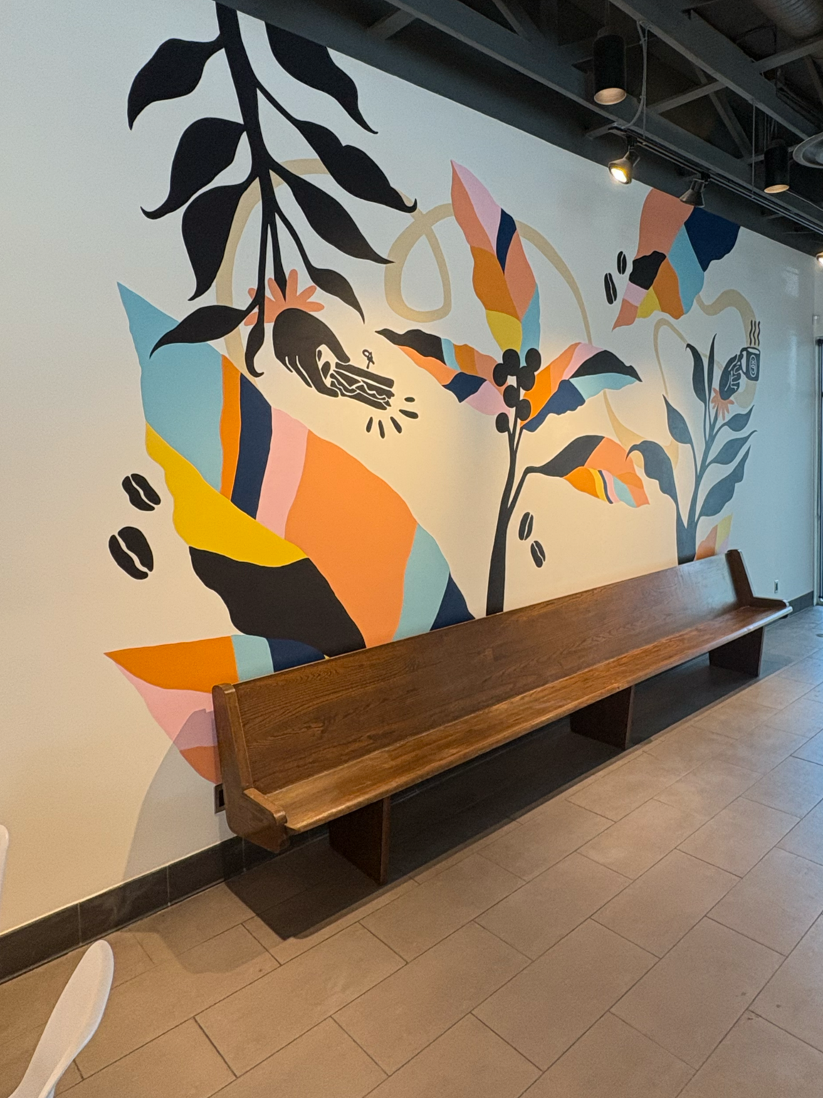 A colorful abstract mural of leaves and plants on a wall with a wooden bench in front.