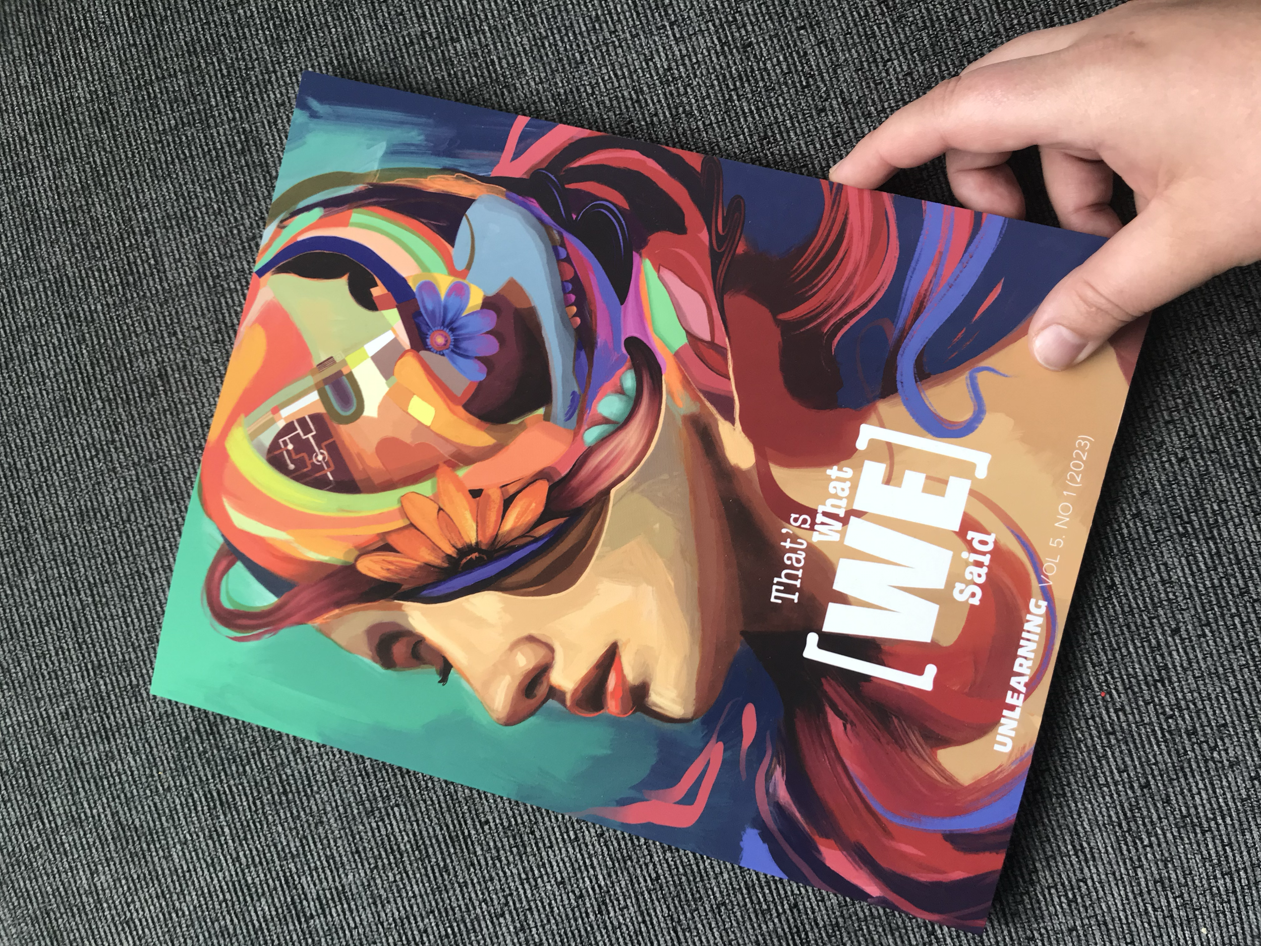 Colorful magazine cover with an abstract painted woman's face and head, decorated with flowers, glasses, and vibrant swirling shapes, featuring the text 'What's WHAT WE' Said' and additional text about unreleased material.