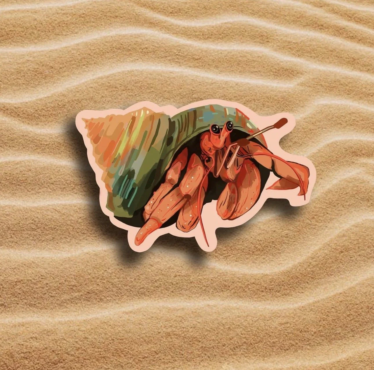A sticker of a hermit crab on sandy ground.